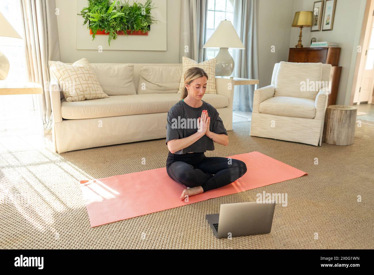 Femme méditant à la maison avec un ordinateur portable Banque D'Images