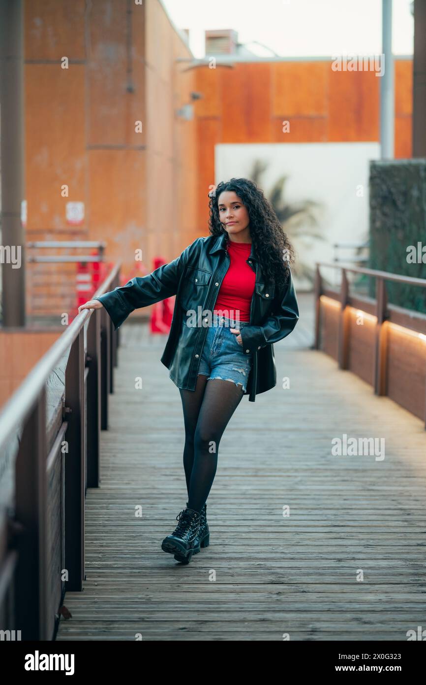 Femme élégante aux cheveux bouclés en tenue décontractée s'appuyant sur une balustrade au crépuscule Banque D'Images