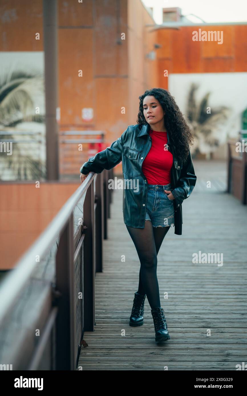 Femme élégante aux cheveux bouclés en tenue décontractée s'appuyant sur une balustrade au crépuscule Banque D'Images