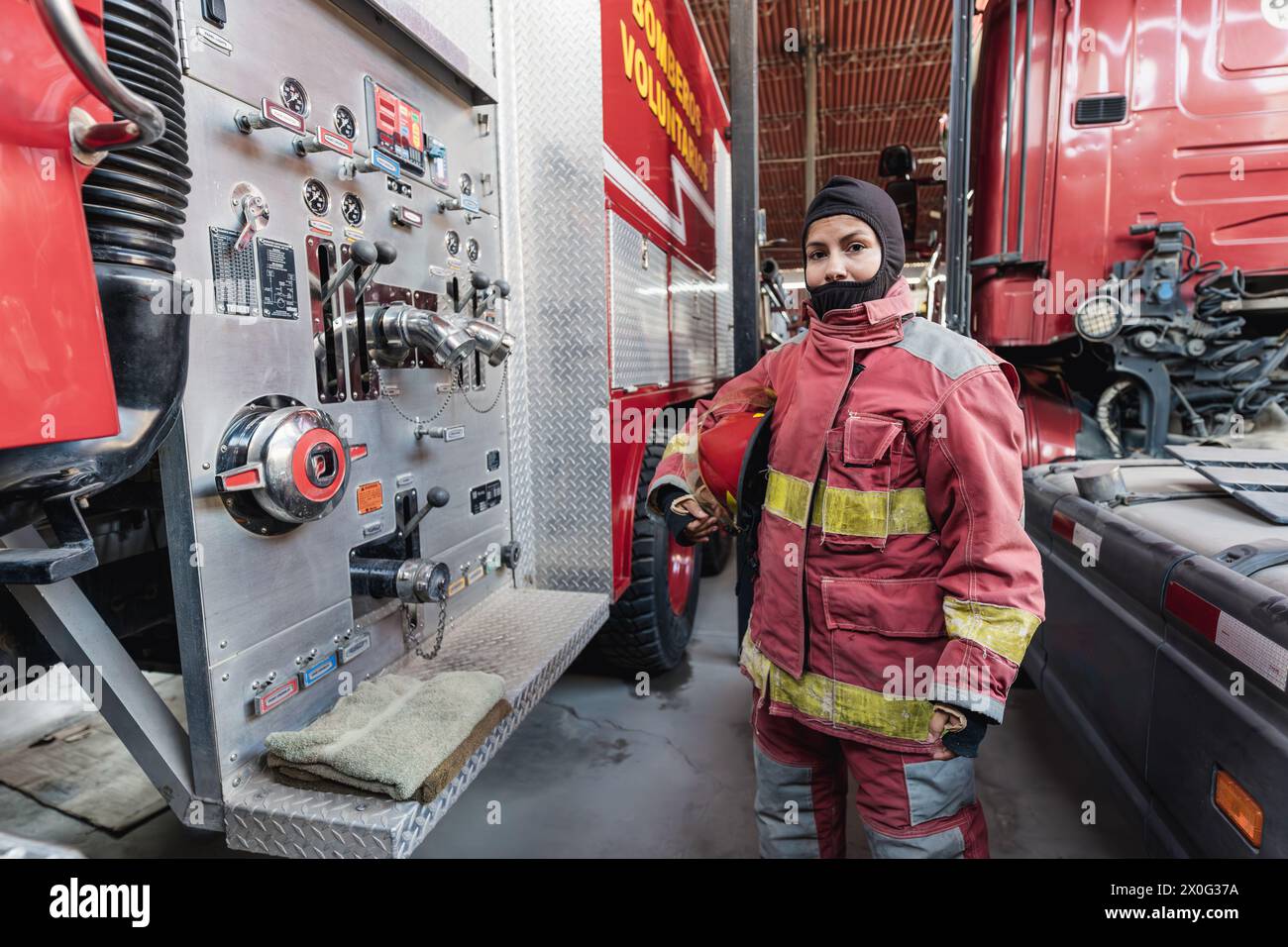 Pompier féminin en costume de protection incendie debout à la caserne de pompiers Banque D'Images