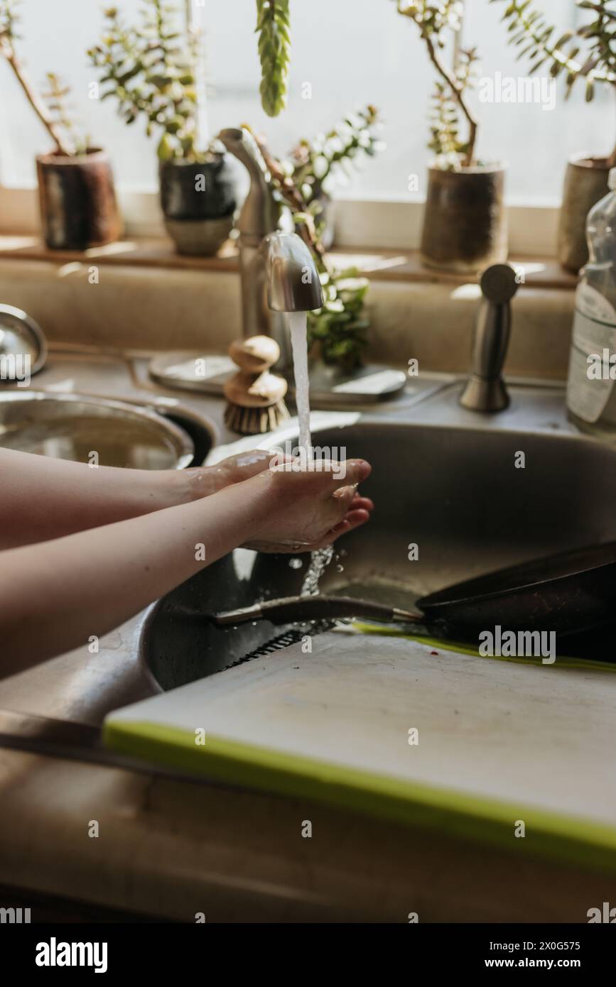 Jeune fille tient les mains sous l'eau courante dans l'évier de cuisine Banque D'Images