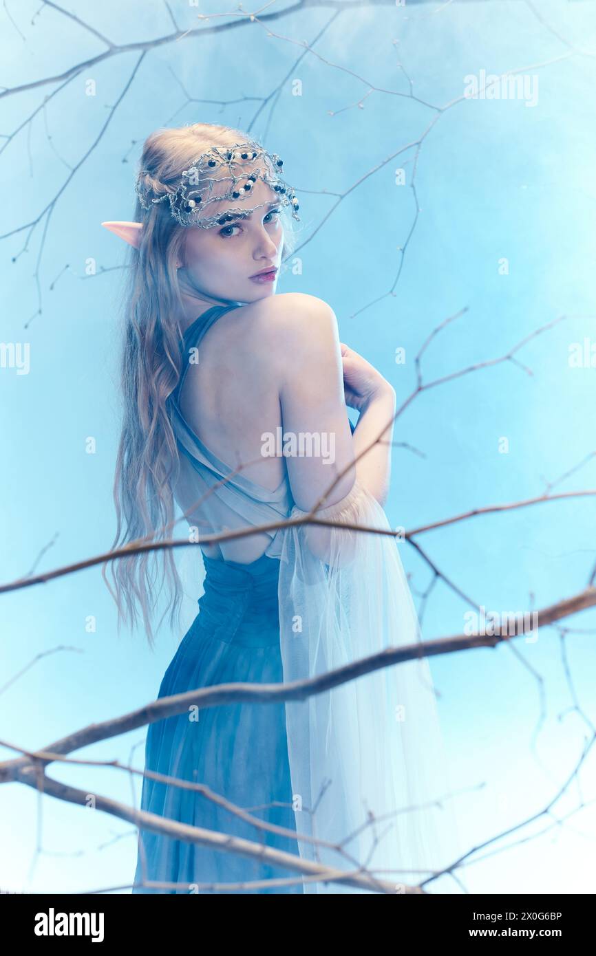 Une jeune femme dans une robe bleue fluide se tient gracieusement dans un arbre, incarnant une princesse fée dans un monde fantastique. Banque D'Images