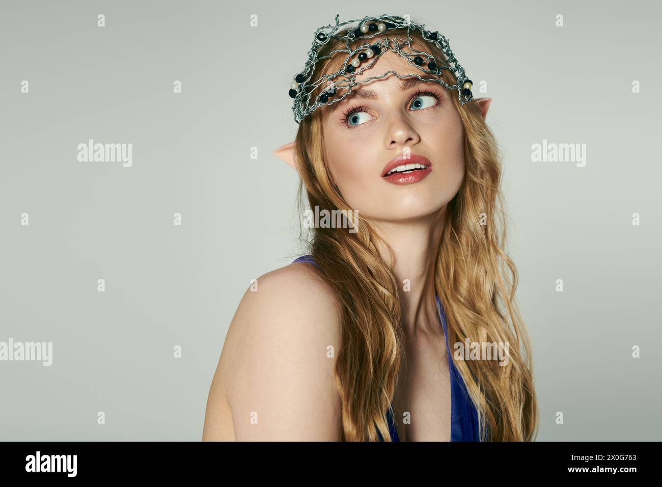 Une jeune femme portant une couronne, incarnant une princesse elfe ressemblant à une fée dans un cadre de studio fantaisiste. Banque D'Images