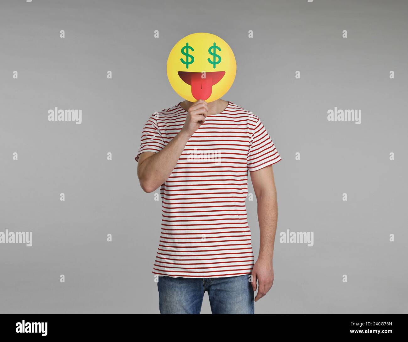 Homme tenant une émoticône avec des signes dollar au lieu des yeux sur fond gris Banque D'Images