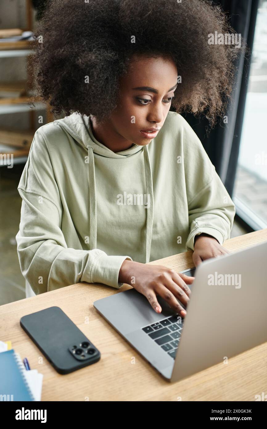 Une femme noire est assise à une table, intensément concentrée sur son ordinateur portable dans un espace de coworking moderne Banque D'Images