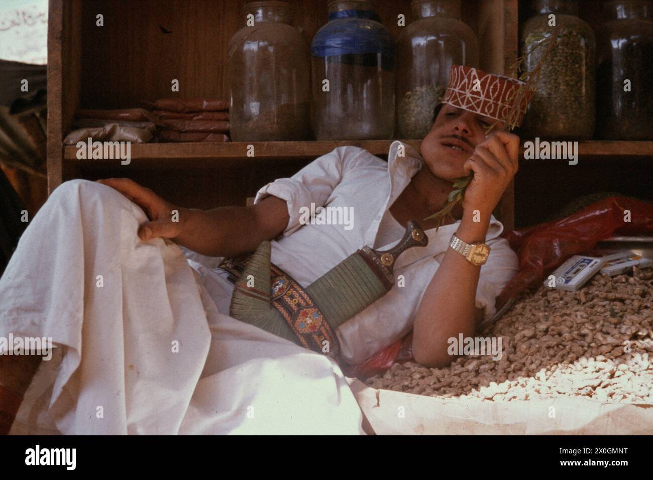 Un homme dans une robe traditionnelle la mastication du khat dans l'ombre dans un souk à Sanaa. Banque D'Images