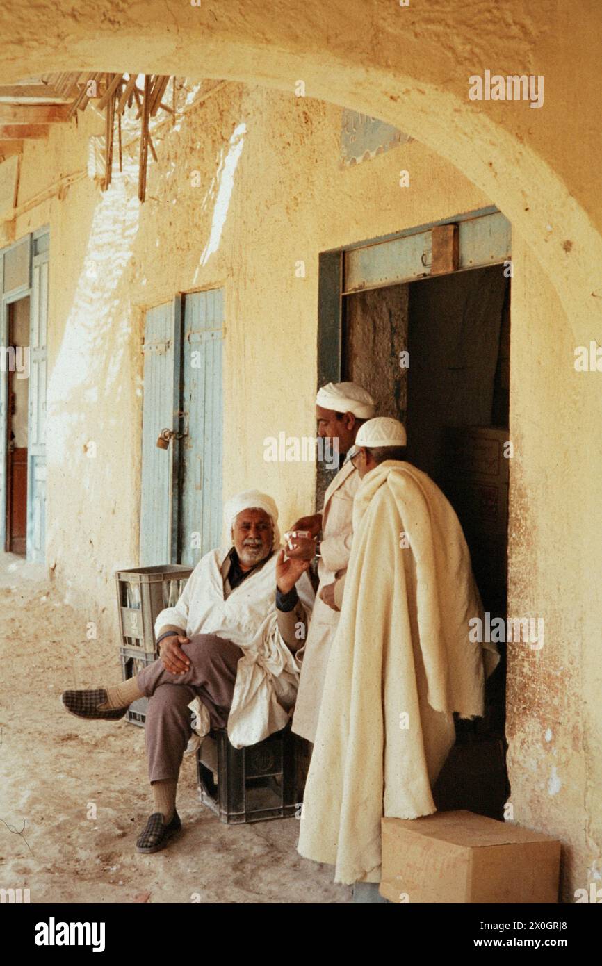 Trois hommes âgés bavardant en face d'arcades sur la place du marché de Touggourt. Banque D'Images
