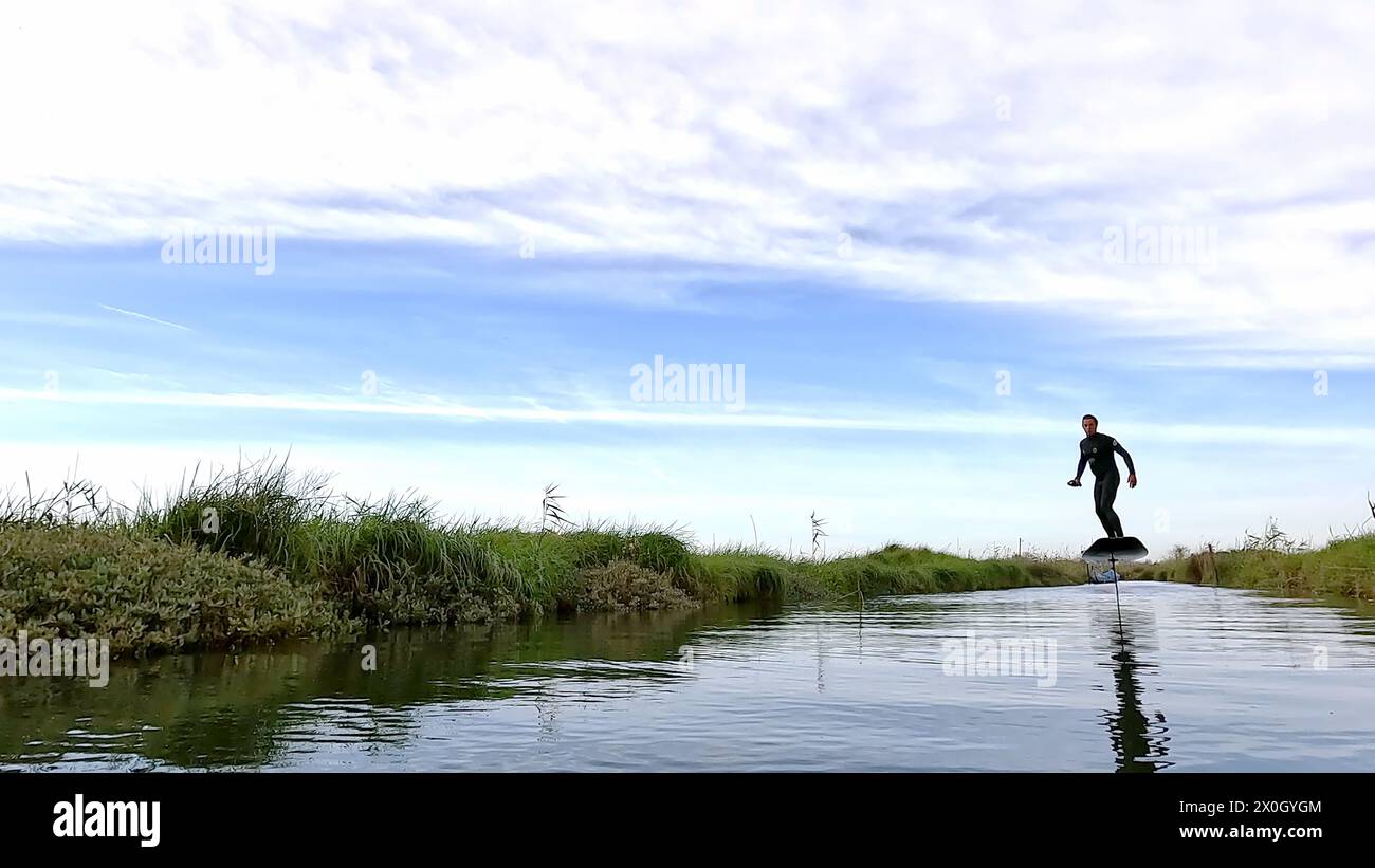 Hydroptère glissant au-dessus de l'eau avec sa planche dans l'un des canaux de la Ria de Aveiro au Portugal par une journée nuageuse. Banque D'Images