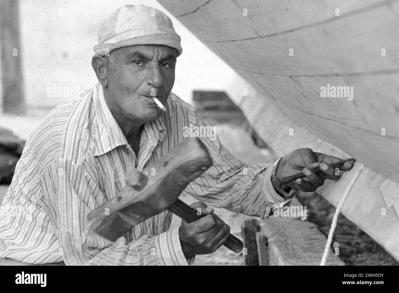 Afin de sceller le bateau, le constructeur de bateaux de Tartus conduit une feuille de remorquage entre les planches de bois. [traduction automatique] Banque D'Images