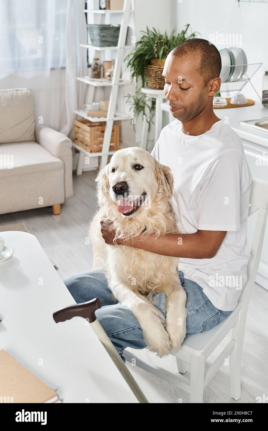 Un Afro-américain handicapé est assis contemplativement dans une chaise, tenant son fidèle chien Labrador à côté de lui. Banque D'Images