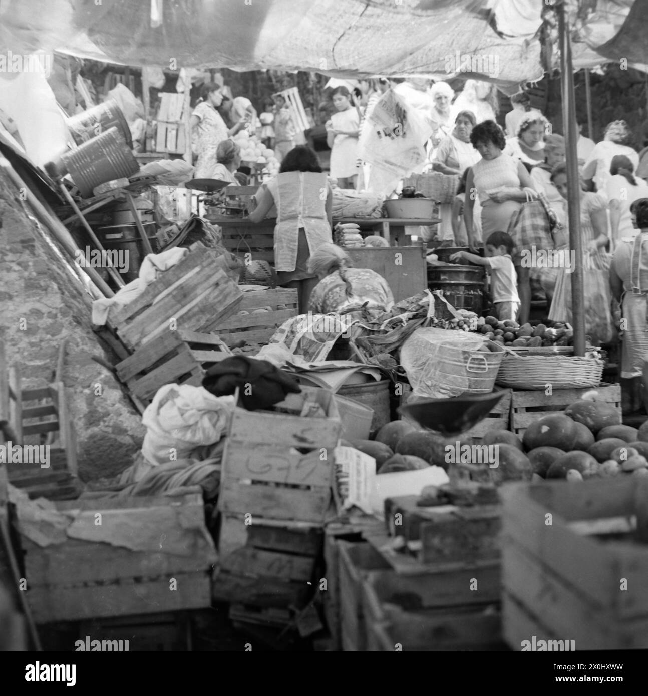 Vue sur un stand de marché à Cuernavaca au Mexique. Derrière le stand, de nombreuses boîtes en bois sont couchées dans un désordre. Entre les caisses sont les commerçants. Devant le stand, les passants se bousquent sur un chemin étroit à travers le marché et regardent les produits offerts. [traduction automatique] Banque D'Images