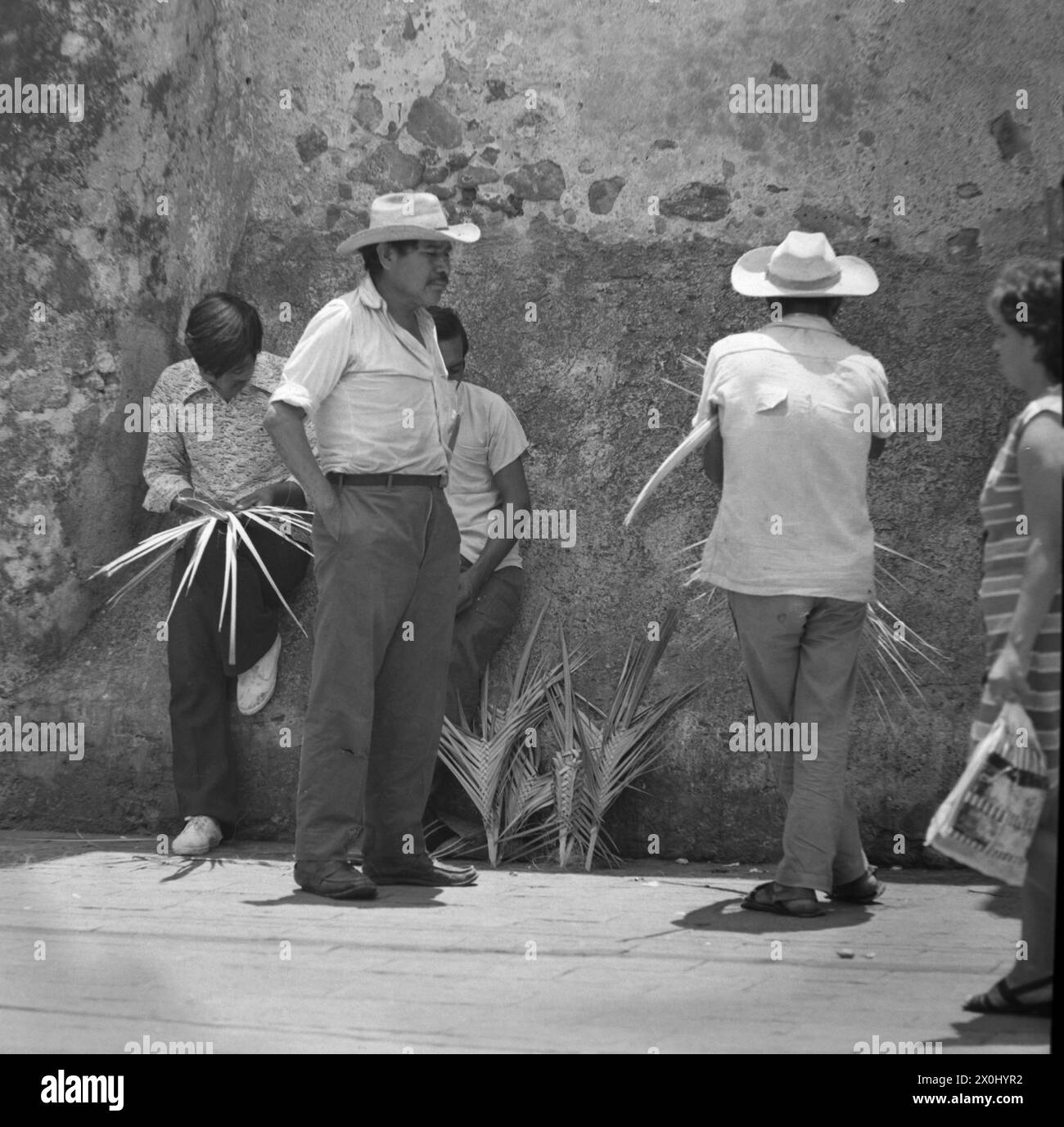Quatre hommes se tiennent ensemble sur un mur à Guernavaca au Mexique. Deux d'entre eux portent des chapeaux avec de larges pots de vin. D'autres sont des feuilles de palmier tressées. [traduction automatique] Banque D'Images