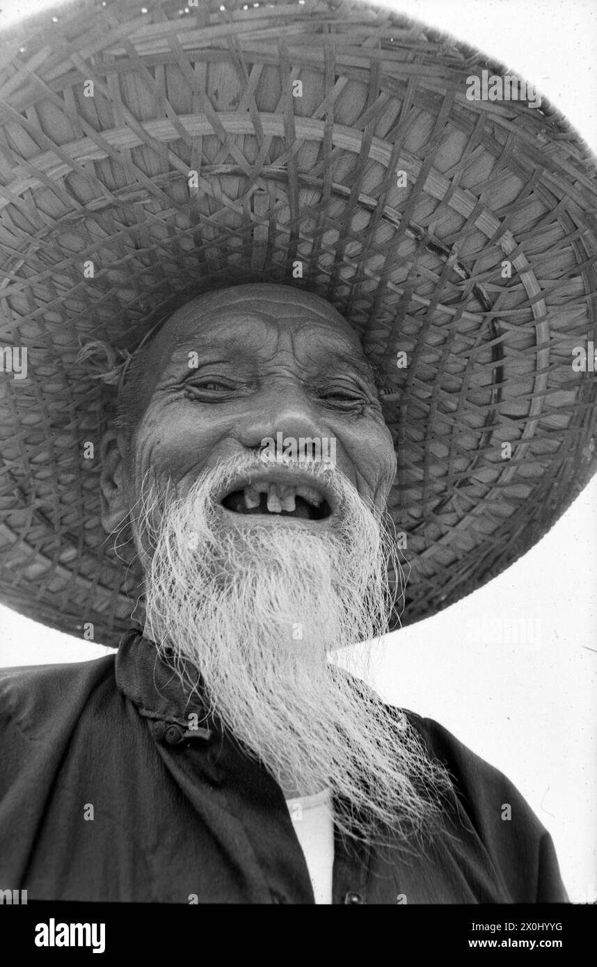 Portrait d'un vieil homme avec une longue barbe blanche et un chapeau de paille à Hong Kong. Il rit. Il manque quelques dents. [traduction automatique] Banque D'Images