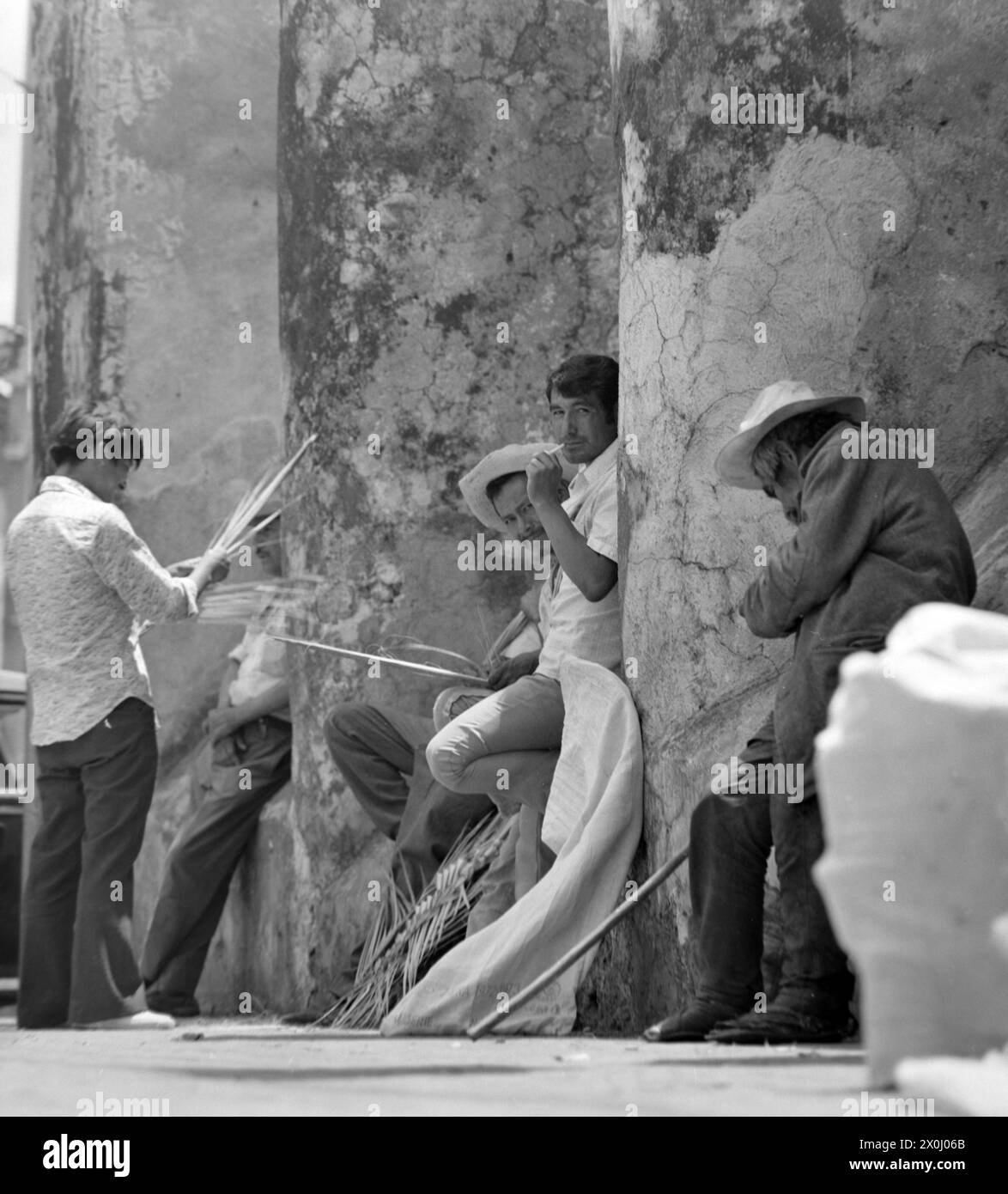 Certains hommes se tiennent ensemble sur un mur à Guernavaca au Mexique. Deux d'entre eux portent des chapeaux avec de larges pots-de-vin. D'autres sont des feuilles de palmier tressées. [traduction automatique] Banque D'Images