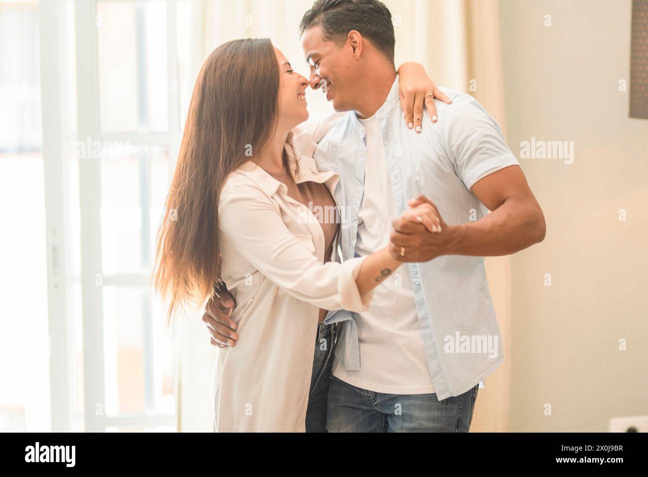 Couple interracial danse à la maison ensemble s'amuser et aimer. Propriétaire de maison neuve et prêt loisir activité intérieure. Garçon et fille en relation ont du plaisir à la maison dansant et souriant l'un à l'autre Banque D'Images