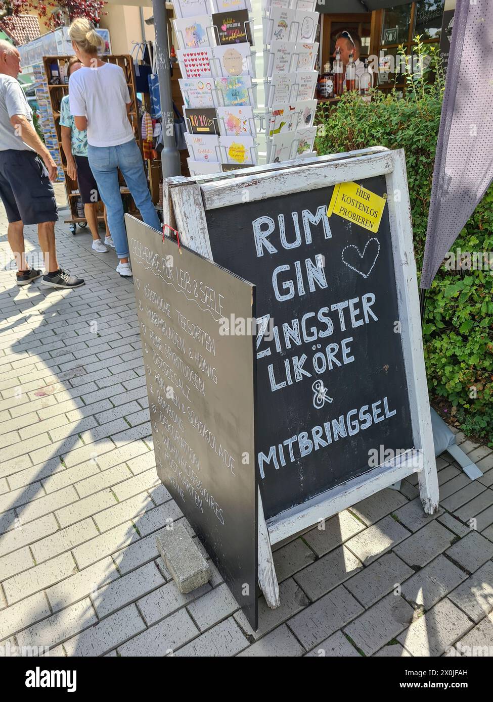 Un panneau publicitaire manuscrit se trouve à l'extérieur du magasin annonçant le rhum, le gin, les souvenirs et les liqueurs de Zingst, les touristes en arrière-plan, Ostseebad Zingst, Allemagne Banque D'Images