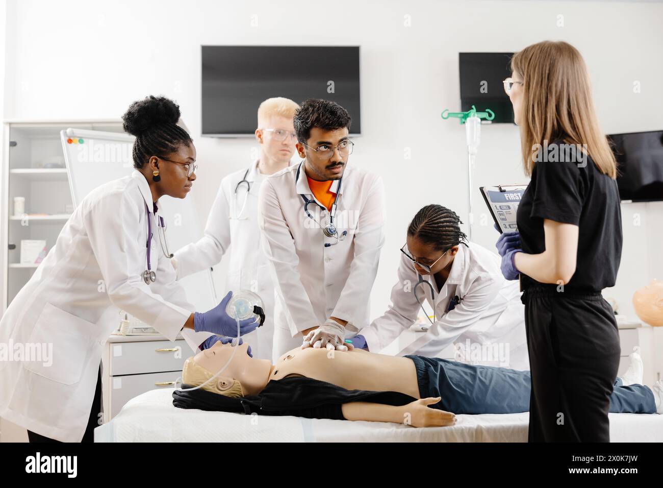 Un groupe de médecins en manteau blanc conversant avec un patient assis sur une table d'examen dans une salle clinique. Banque D'Images
