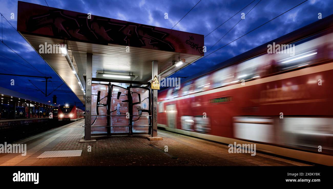 trafic ferroviaire avec trains arrivant et partant sur le quai de la gare de cologne ehrenfeld au crépuscule Banque D'Images