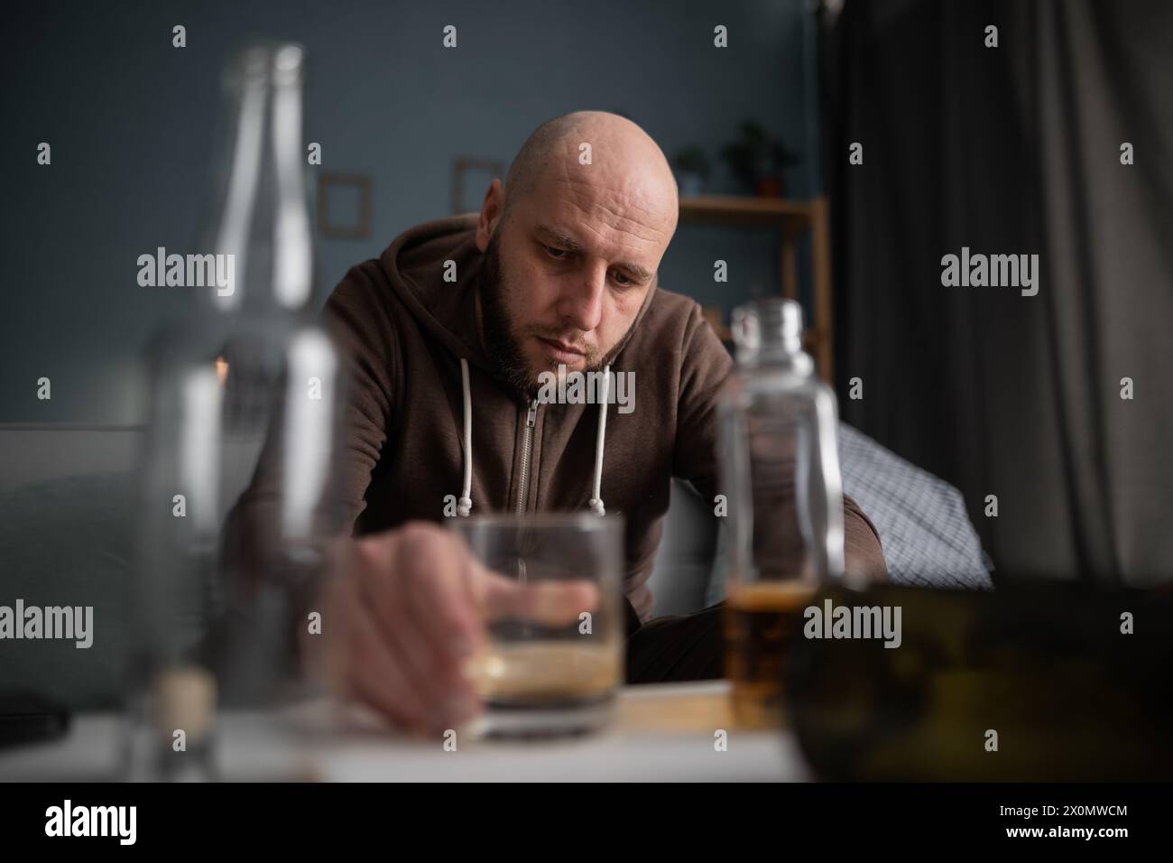 Homme ivre ou homme alcoolique buvant whisky à la maison assis entre de nombreuses bouteilles. Alcoolisme, alcoolisme et toxicomanie et personnes Banque D'Images