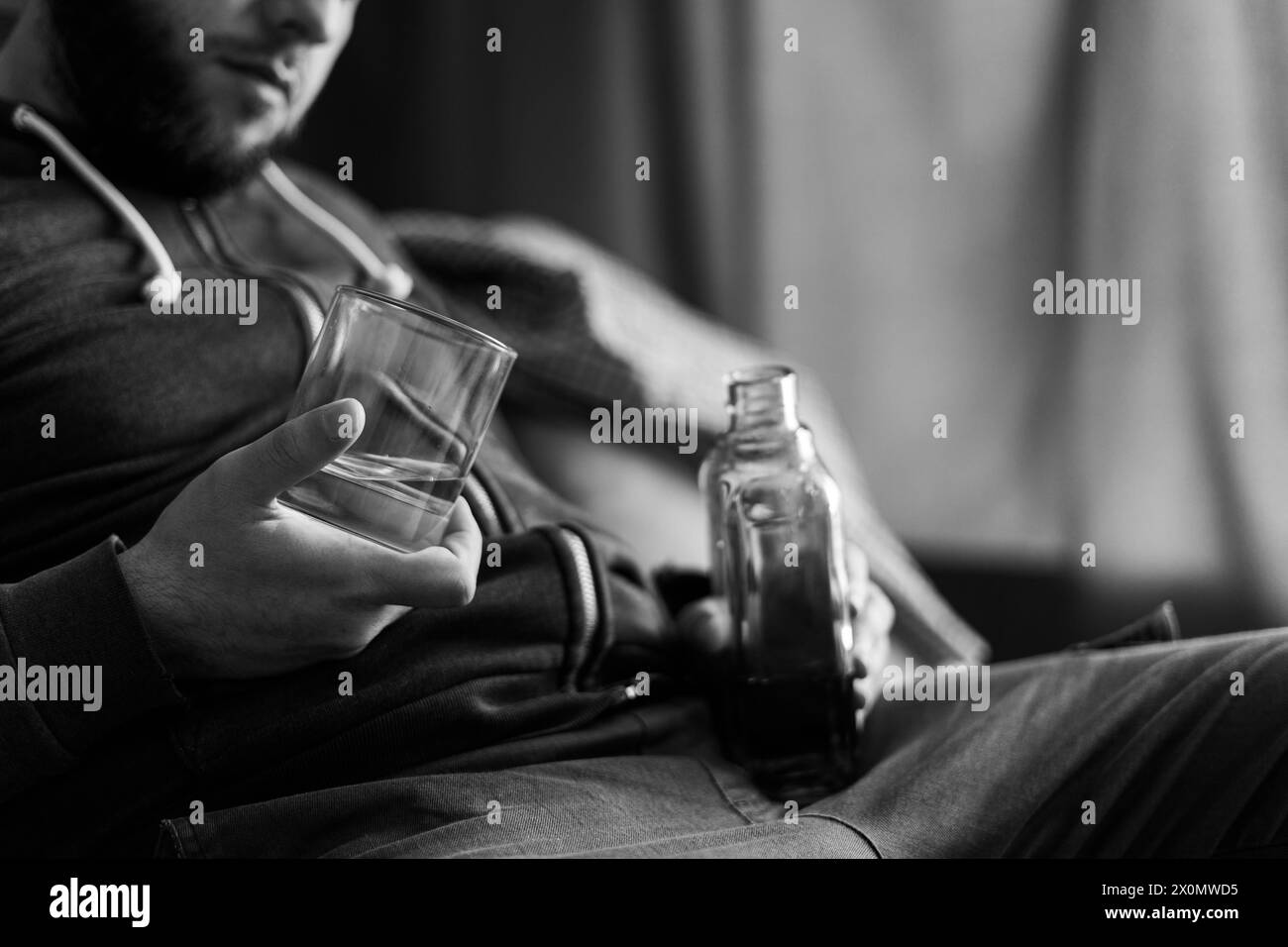 Homme ivre et solitaire tenant une bouteille de whisky et un verre assis sur le canapé, gros plan. abus d'alcoolisme, concept d'alcoolisme Banque D'Images