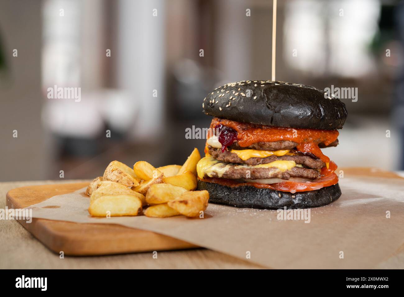 Délicieux Burger de bœuf noir dans du pain avec patty, ketchup et fromage cheddar sur planche de bois. Restaurant de restauration rapide Banque D'Images