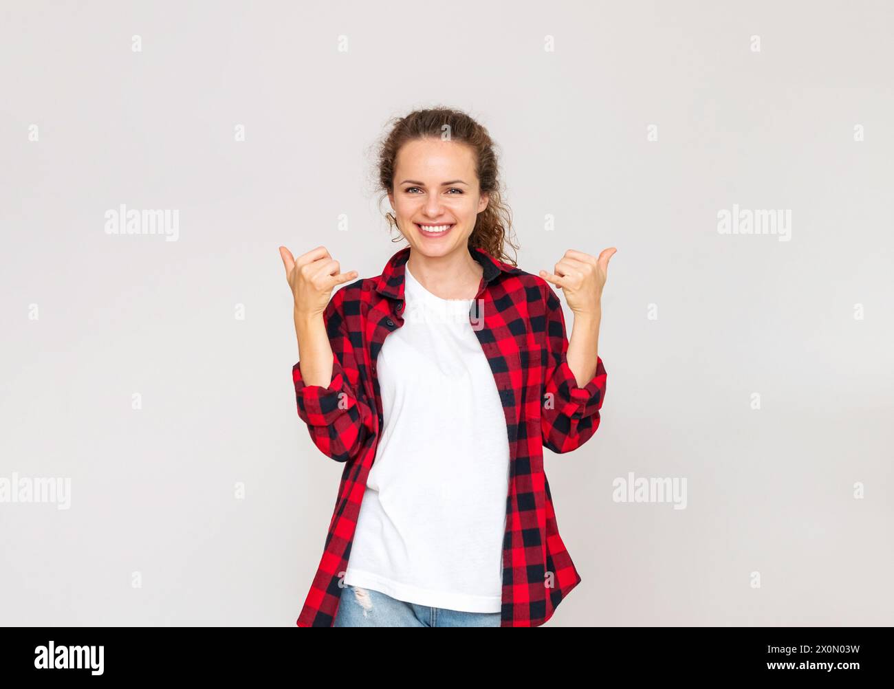 Femme joyeuse portant une tenue décontractée sourires et gestes Shaka signe devant un fond Uni. Banque D'Images