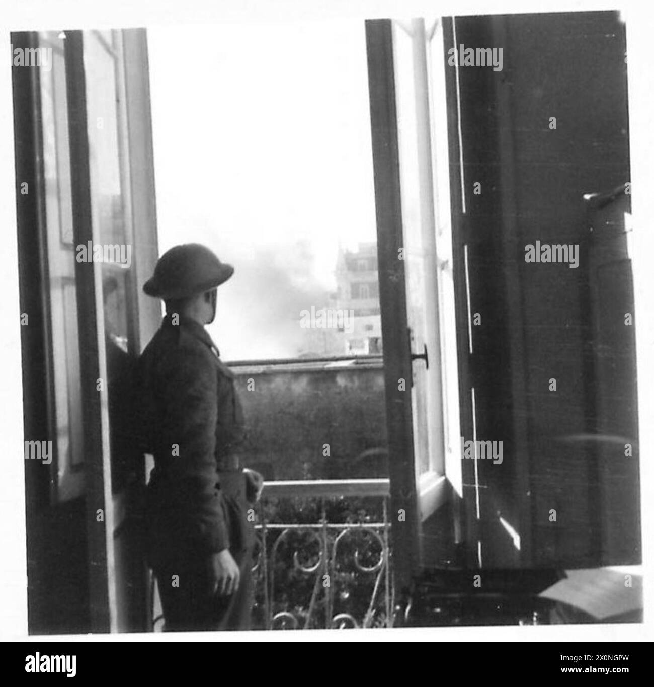 Pilote A. Green regarde depuis une fenêtre comme un obus atterrit à court dans la ville pendant les opérations de l'armée britannique en Afrique du Nord, en Sicile, en Italie, dans les Balkans et en Autriche, 1942-1946. Banque D'Images