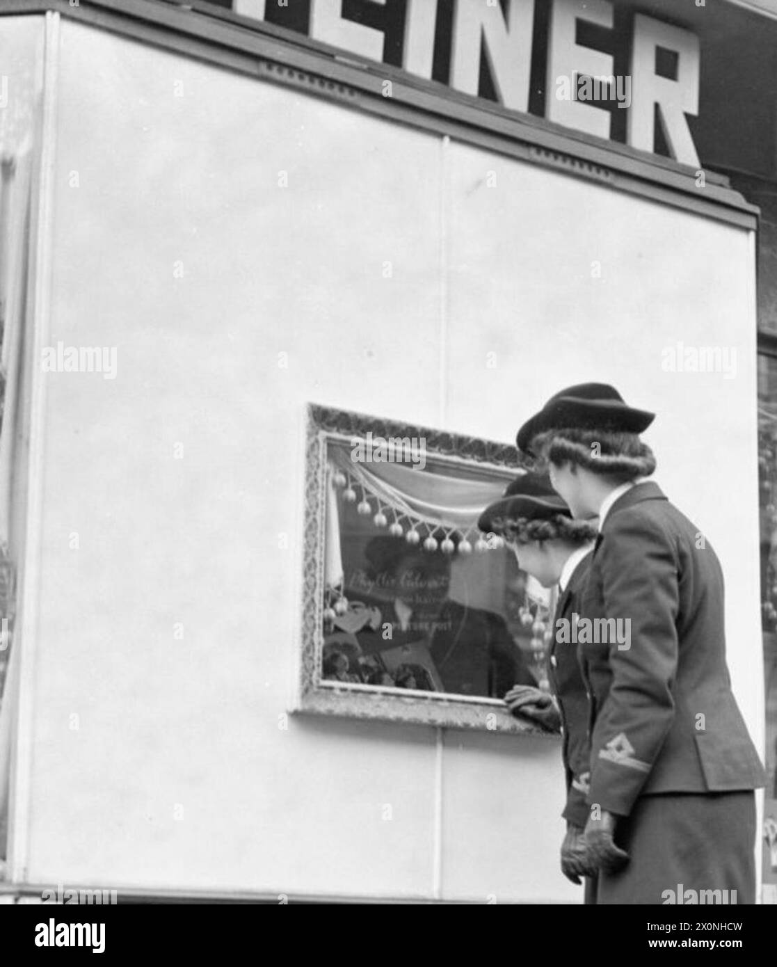 COIFFEUR EN TEMPS DE GUERRE : LE TRAVAIL DU SALON DE STEINER, GROSVENOR STREET, LONDRES, ANGLETERRE, ROYAUME-UNI, 1944 - deux membres du Women's Royal Naval Service regardent par la fenêtre du salon de coiffure Steiner sur Grosvenor Street, Londres. La fenêtre est petite et est un cadre photo au centre d'une fenêtre plus grande, maintenant embarqué vers le haut après les dommages causés par l'explosion. Steiner's avait été bombardé hors de leurs locaux précédents Banque D'Images