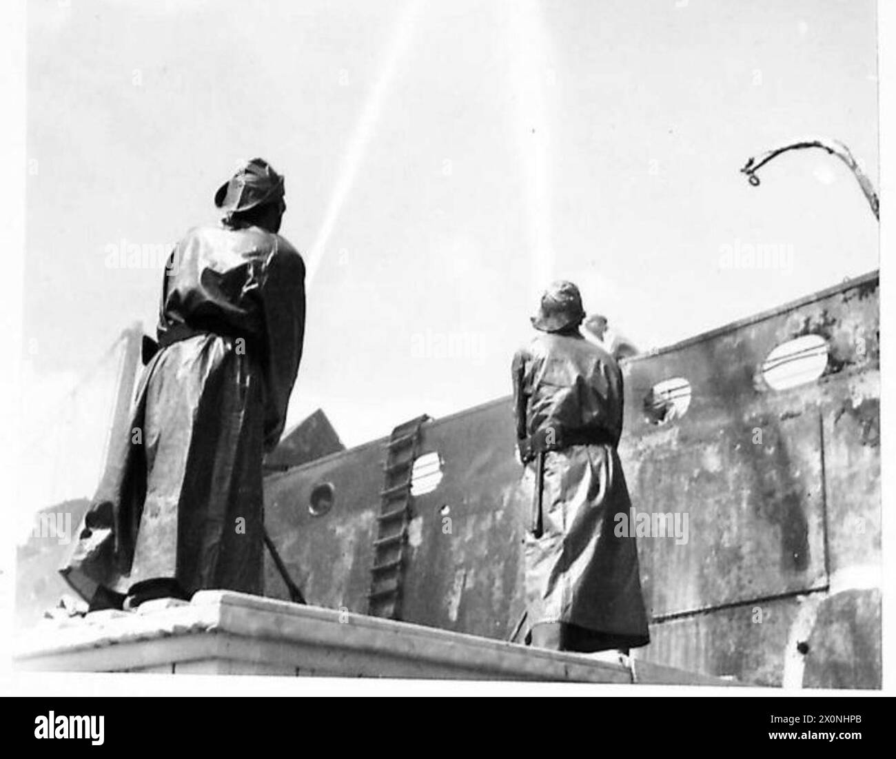 Deux pompiers de l'armée utilisent des tuyaux à angle élevé pour atteindre les flammes sur les ponts d'un navire en feu à Trieste. Banque D'Images