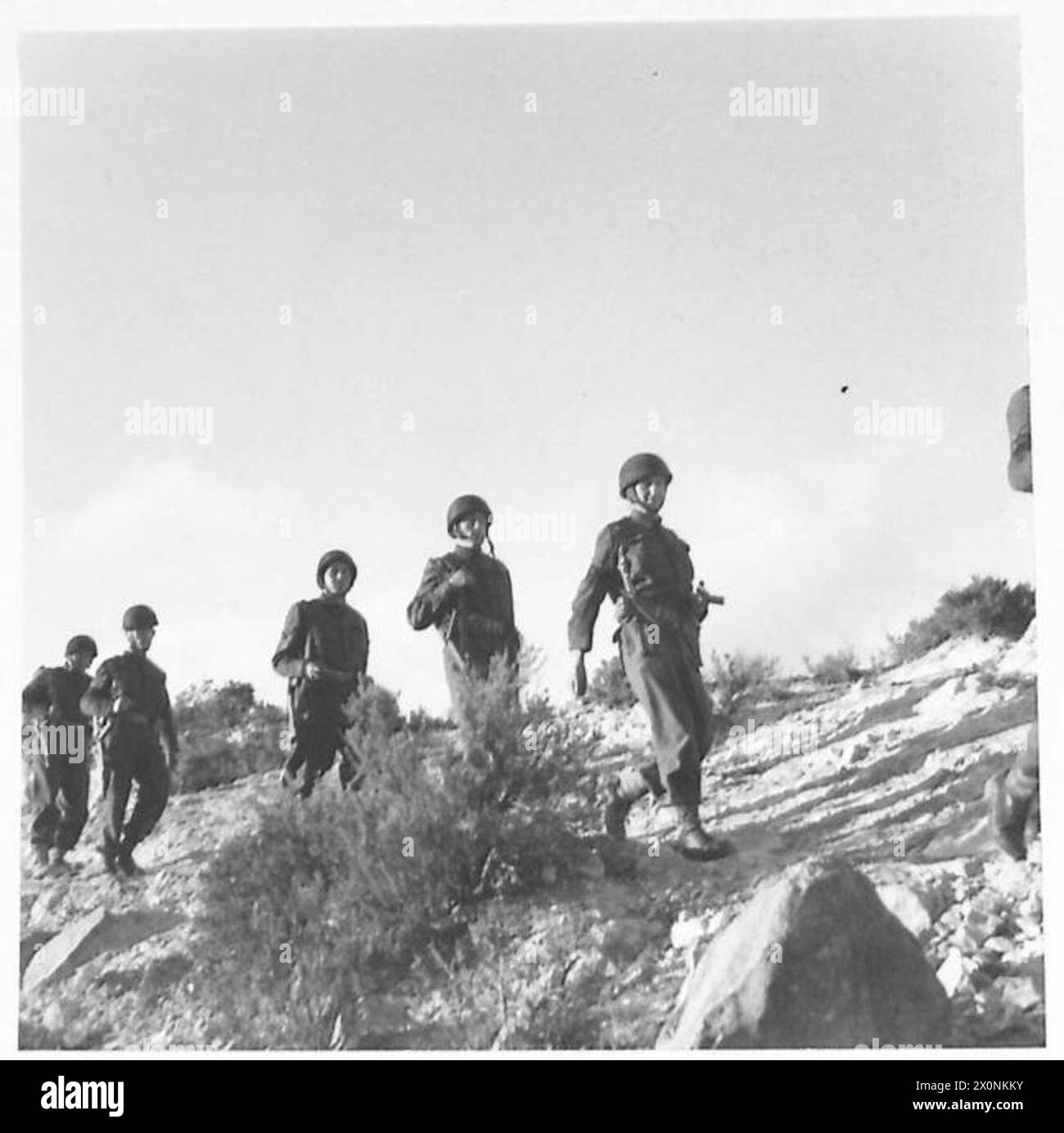 L'ARMÉE BRITANNIQUE DANS LA CAMPAGNE DE TUNISIE, NOVEMBRE 1942-MAI 1943 - Major Price et police de la Provost se dirigeant sur le flanc de la montagne en direction du village. Deux sous-sections d'une compagnie de prévôt divisionnaire dirigée par le major Price APM et assistée d'un officier français et de deux policiers militaires français sont allés attaquer un village arabe situé dans la chaîne de montagnes qui sépare Teboursouk d'El Aroussa alors que des traînards allemands et italiens étaient soupçonnés de s'y cacher. Après avoir entouré l'endroit et fouillé chaque gobi (hutte) soigneusement les résultats étaient nuls, à l'exception d'un fusil français. Deux civili arabes Banque D'Images