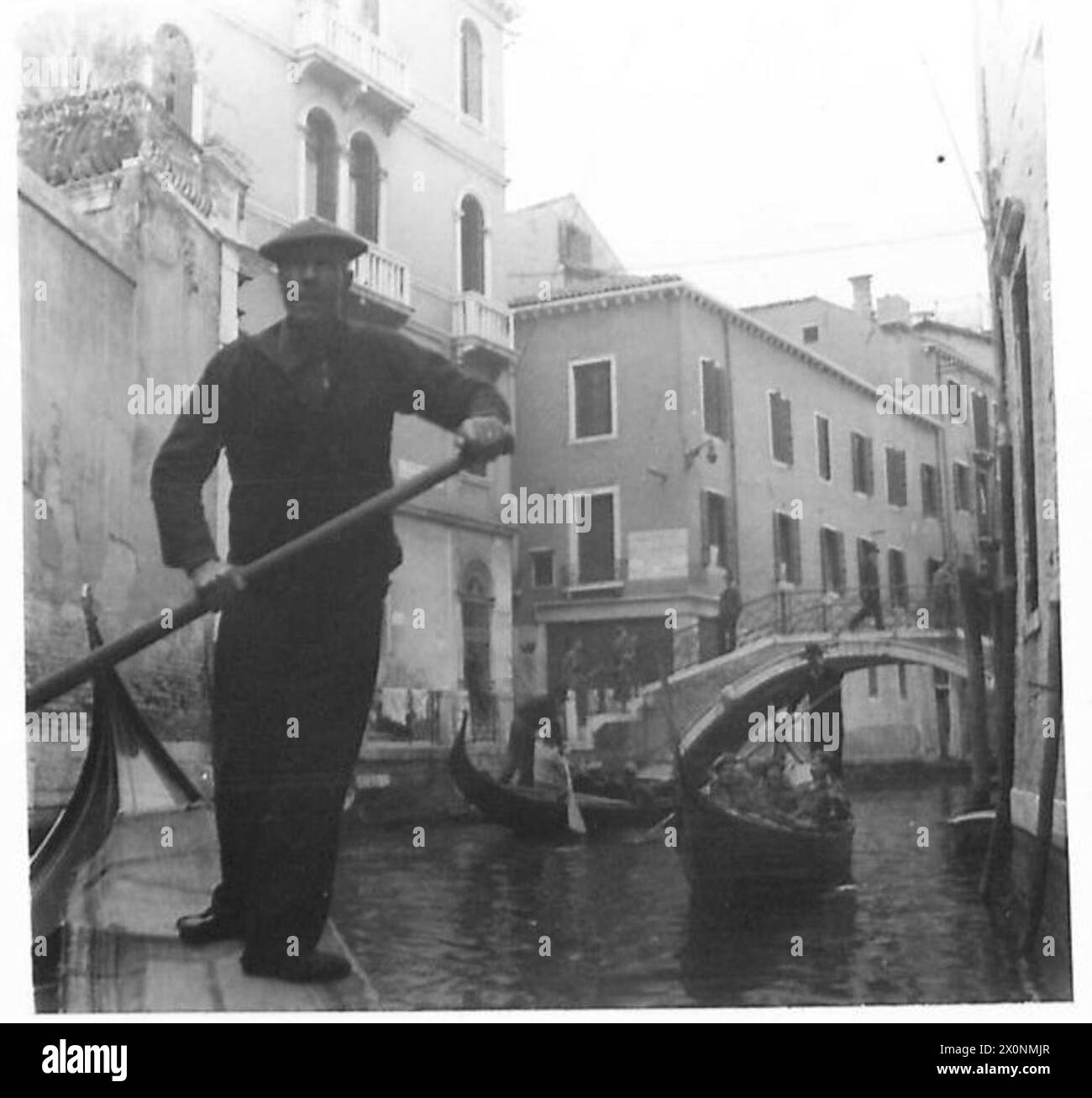 Un soldat de l'armée britannique traverse une étroite rue vénitienne, capturant un moment de la vie quotidienne à Venise pendant la seconde Guerre mondiale. La photographie offre un aperçu de l’environnement urbain rencontré par les troupes stationnées dans la ville. Banque D'Images