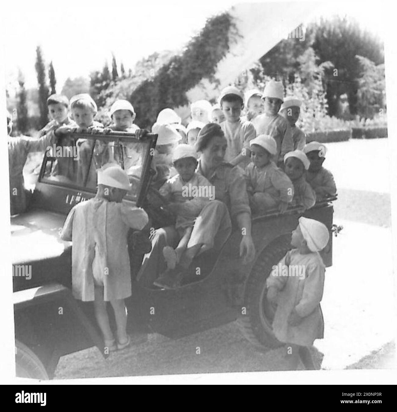 Des enfants montent sur une jeep pour recevoir de la nourriture fournie par l'UNRRA dans un orphelinat. Banque D'Images