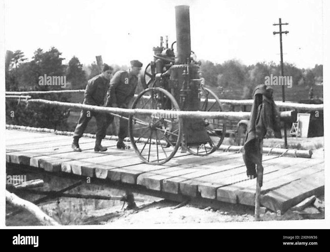 Deux hommes déplacent une pompe à vapeur portative sur un pont temporaire en bois sur un chemin de fer militaire utilisé pour l'entraînement. Banque D'Images
