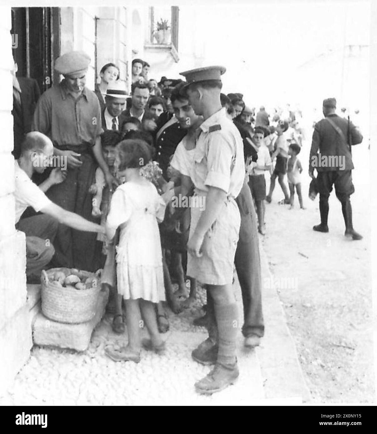 Photographie montrant un boulanger servant des enfants d'une foule sous surveillance militaire pendant l'invasion alliée de la Sicile. Banque D'Images