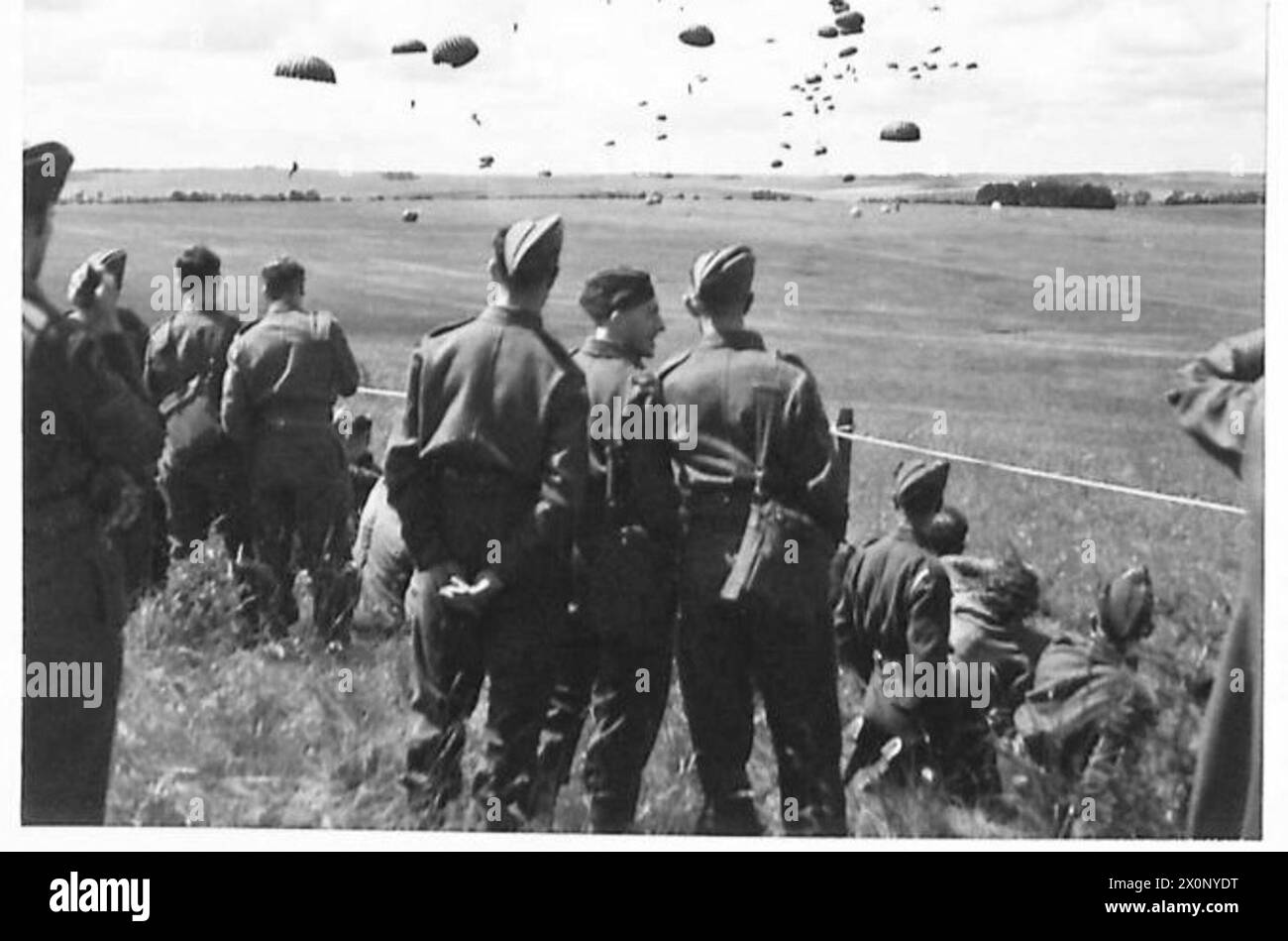 Des soldats de l'armée britannique regardent des parachutistes descendre d'avions lors d'une manifestation pour les ouvriers d'usine. La photographie documente l'entraînement aéroporté et l'engagement du public. Banque D'Images