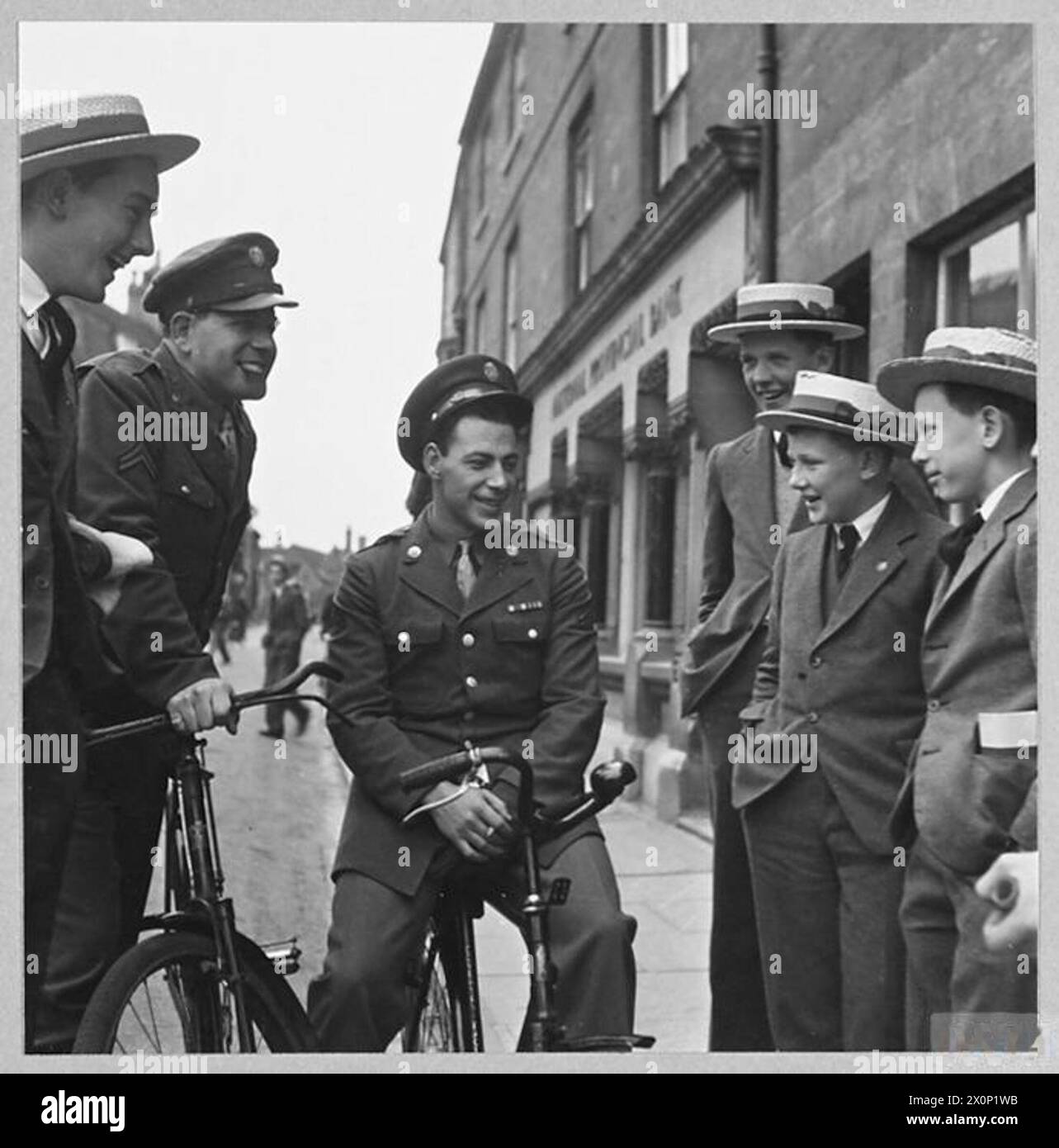 Des soldats américains conversent avec des garçons dans une ferme en 1944, mettant en évidence les interactions entre le personnel militaire et les jeunes locaux. Banque D'Images