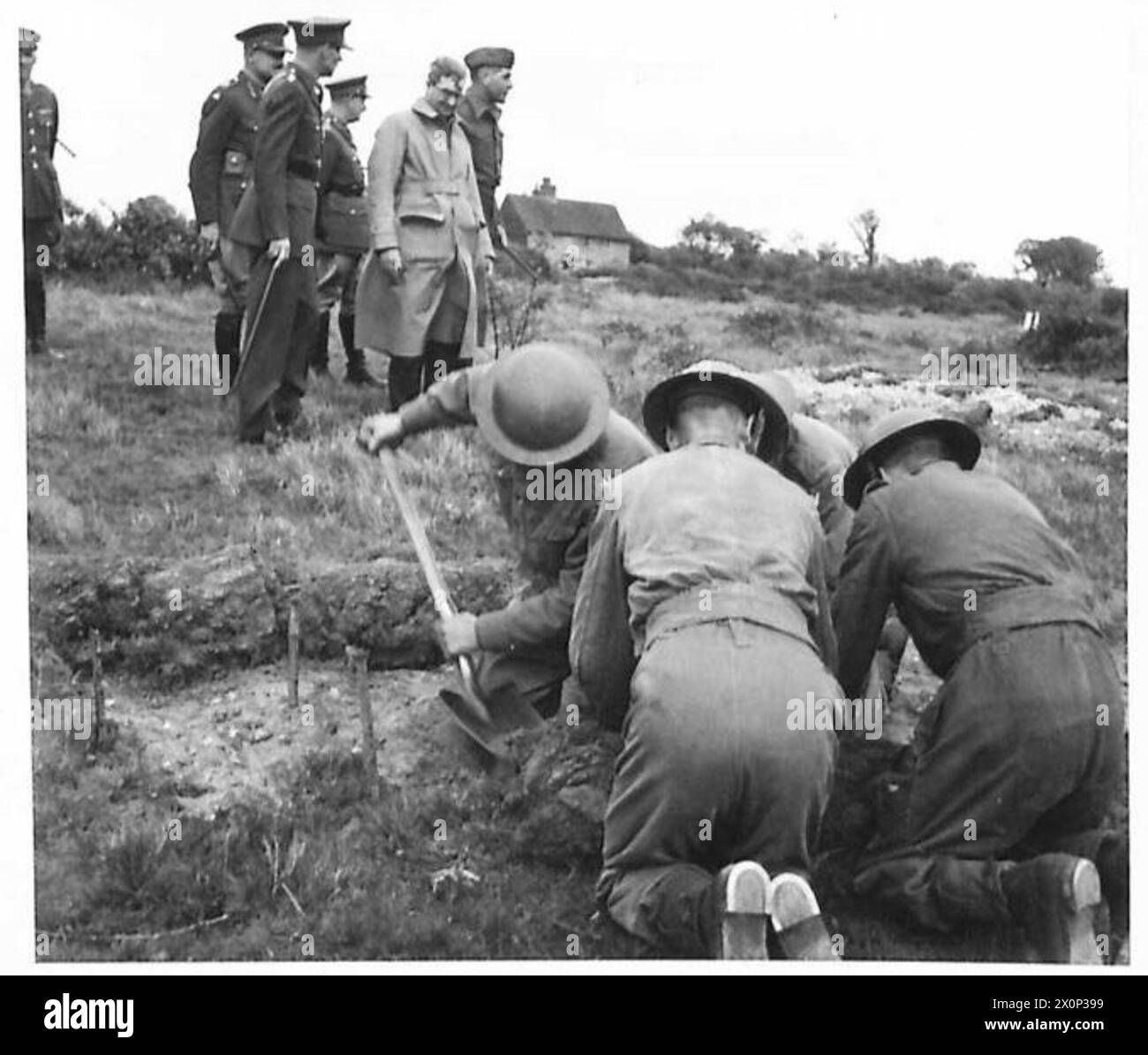 Les troupes creusent des fentes d'armes défensives tout en étant observées par Sir James Grigg, secrétaire d'État à la Guerre, lors d'une visite militaire. Banque D'Images