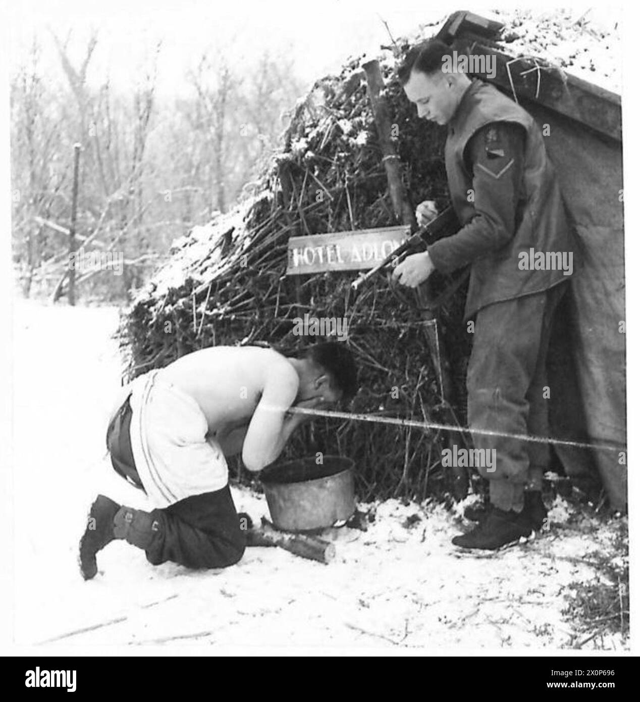 Au cours d'un cours de patrouille de combat, un soldat inspecte son fusil Tommy tandis que son camarade se lave dans de l'eau glacée. Banque D'Images