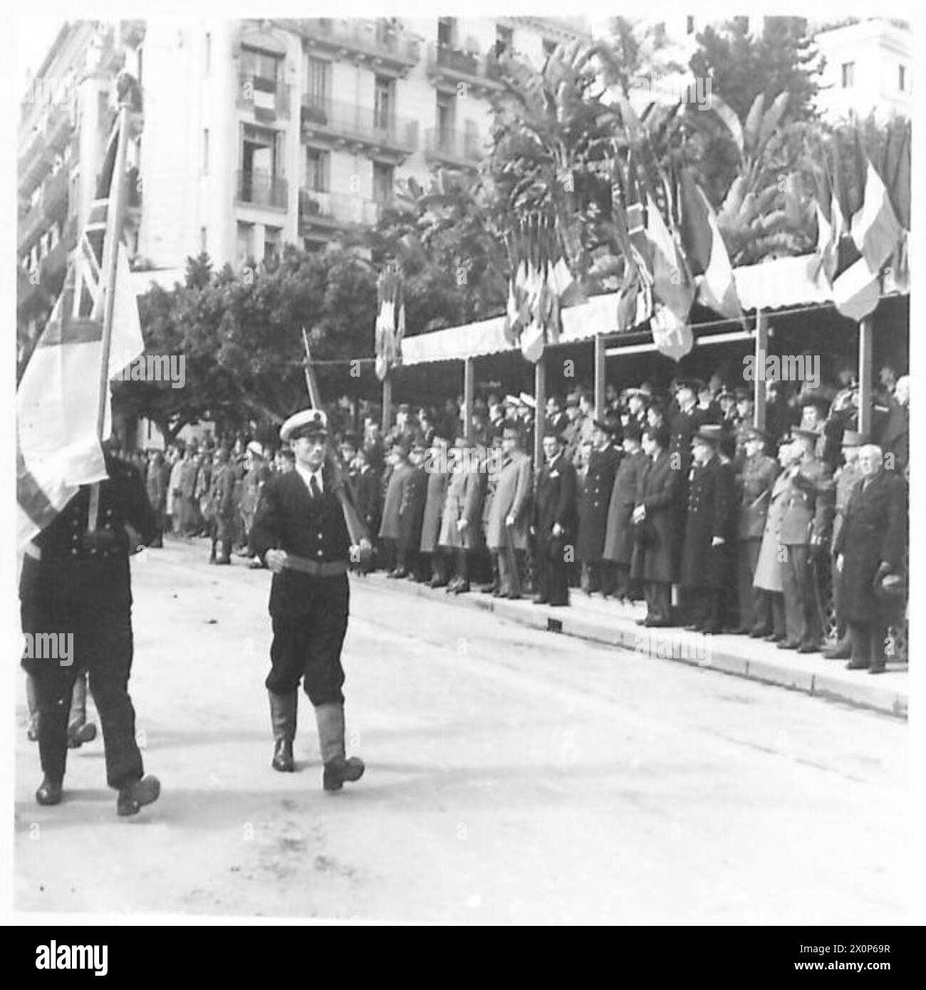 Pendant les célébrations de la Journée de l'Armée rouge à Alger, l'enseigne blanche du contingent naval britannique passe devant la base de salutation. Le négatif photographique documente l'événement cérémonial. Banque D'Images