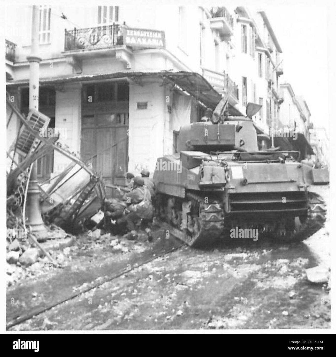 Un char fournit une couverture aux parachutistes cherchant les ruines d'une maison dynamitée en Grèce à la recherche de mines cachées pendant les opérations de guerre civile. Banque D'Images