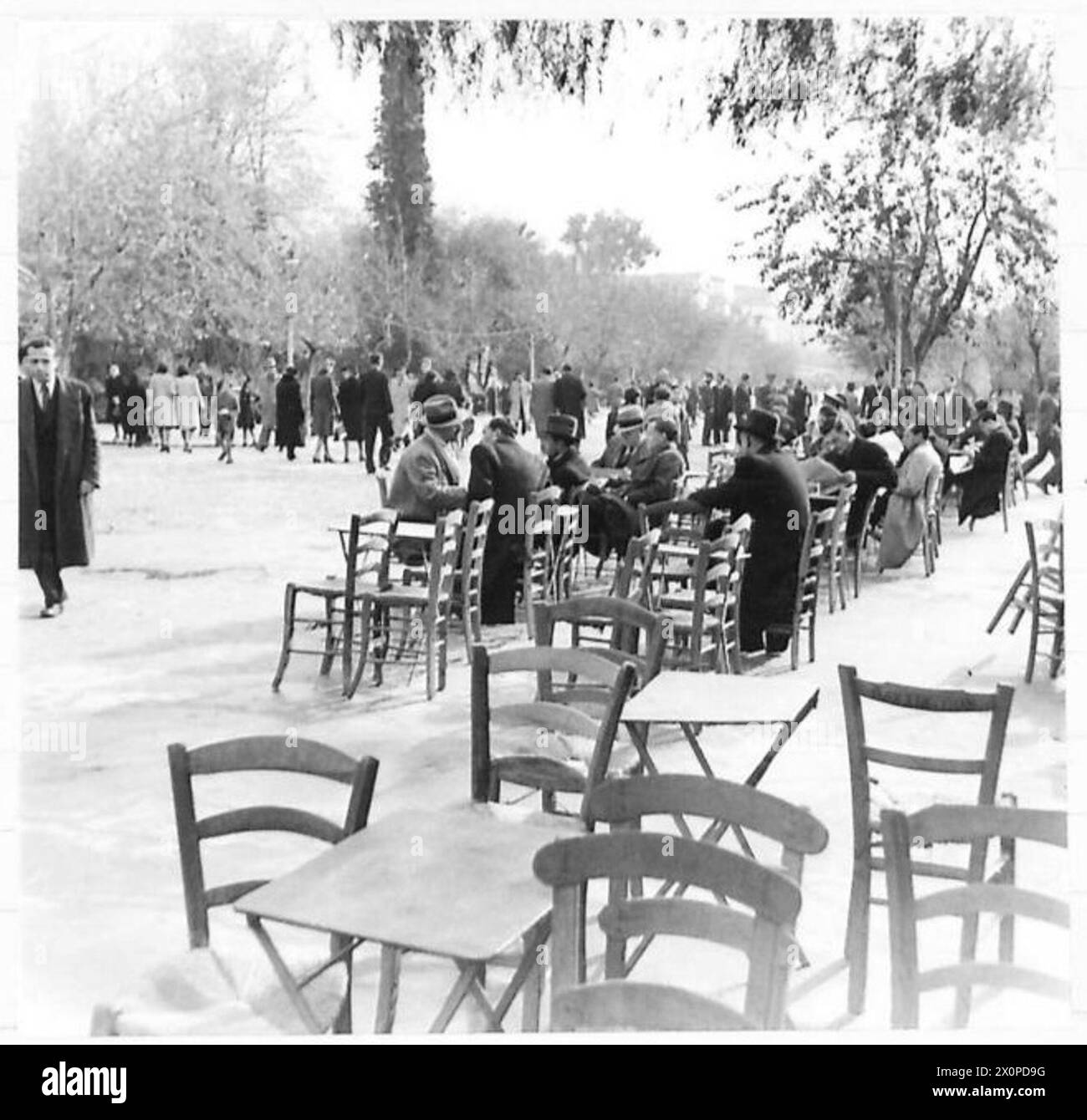 Les gens se détendent dans un parc à Athènes en profitant du soleil avec des chaises et des tables disposées pour le café du matin. Banque D'Images