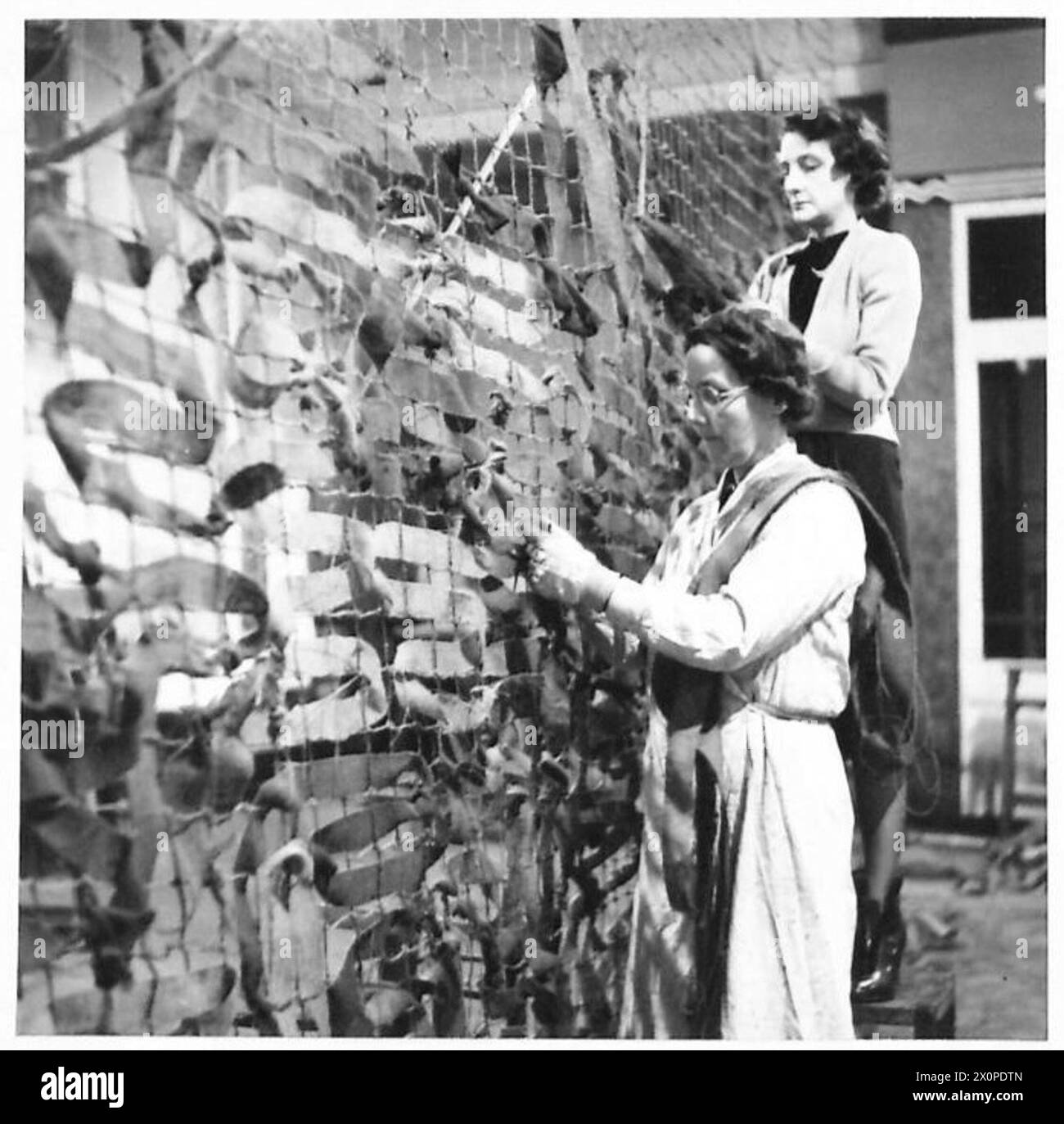 Les femmes fabriquent des filets de camouflage à usage militaire. Banque D'Images