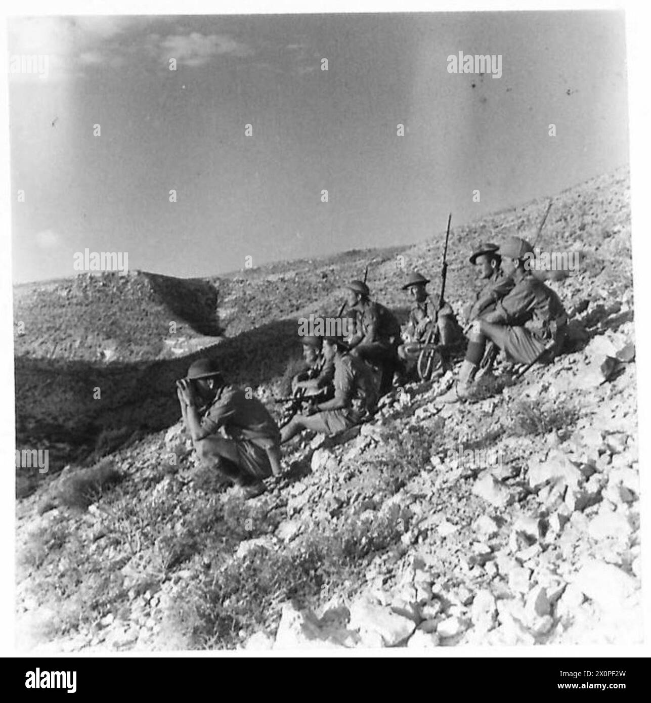 Au cours d'une patrouille à l'aube à Tobrouk, officiers et soldats se reposent tout en se dirigeant vers les positions ennemies. L'officier responsable observe l'activité ennemie à l'aide de jumelles. Banque D'Images