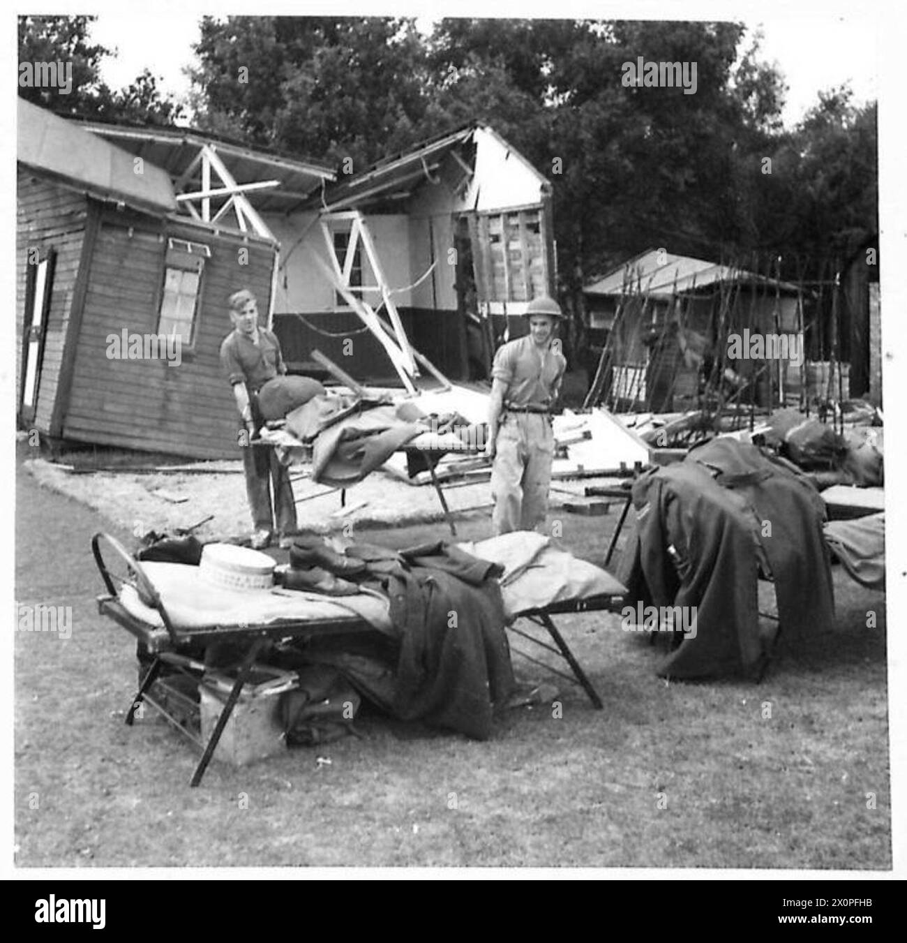 Des artilleurs antiaériens détruisent un avion sans pilote pendant que le personnel retire les effets personnels des cabanes endommagées par la bombe sur le site. Négatif photographique, armée britannique. Banque D'Images