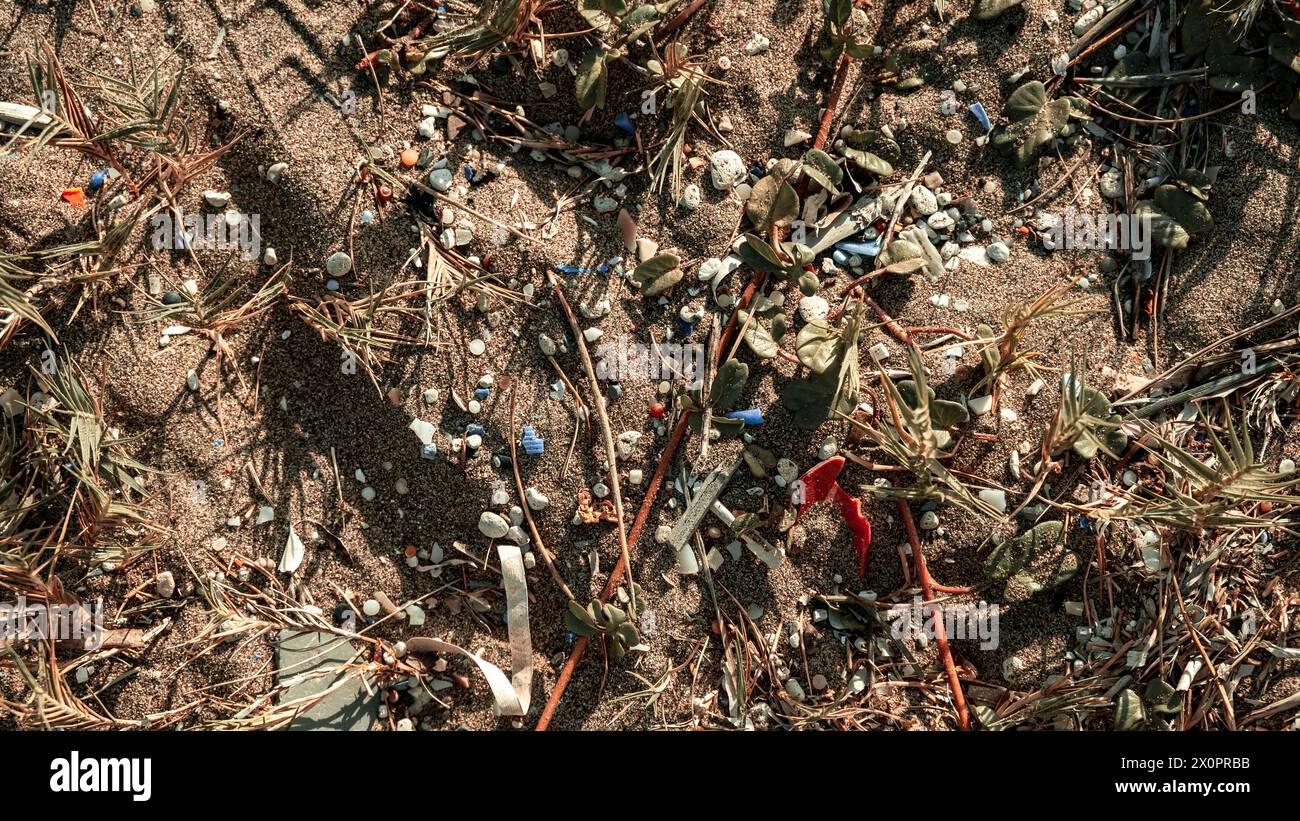 Vue de dessus du sable avec végétation et microplastiques. Le problème des microplastiques réchauffant la planète. Banque D'Images