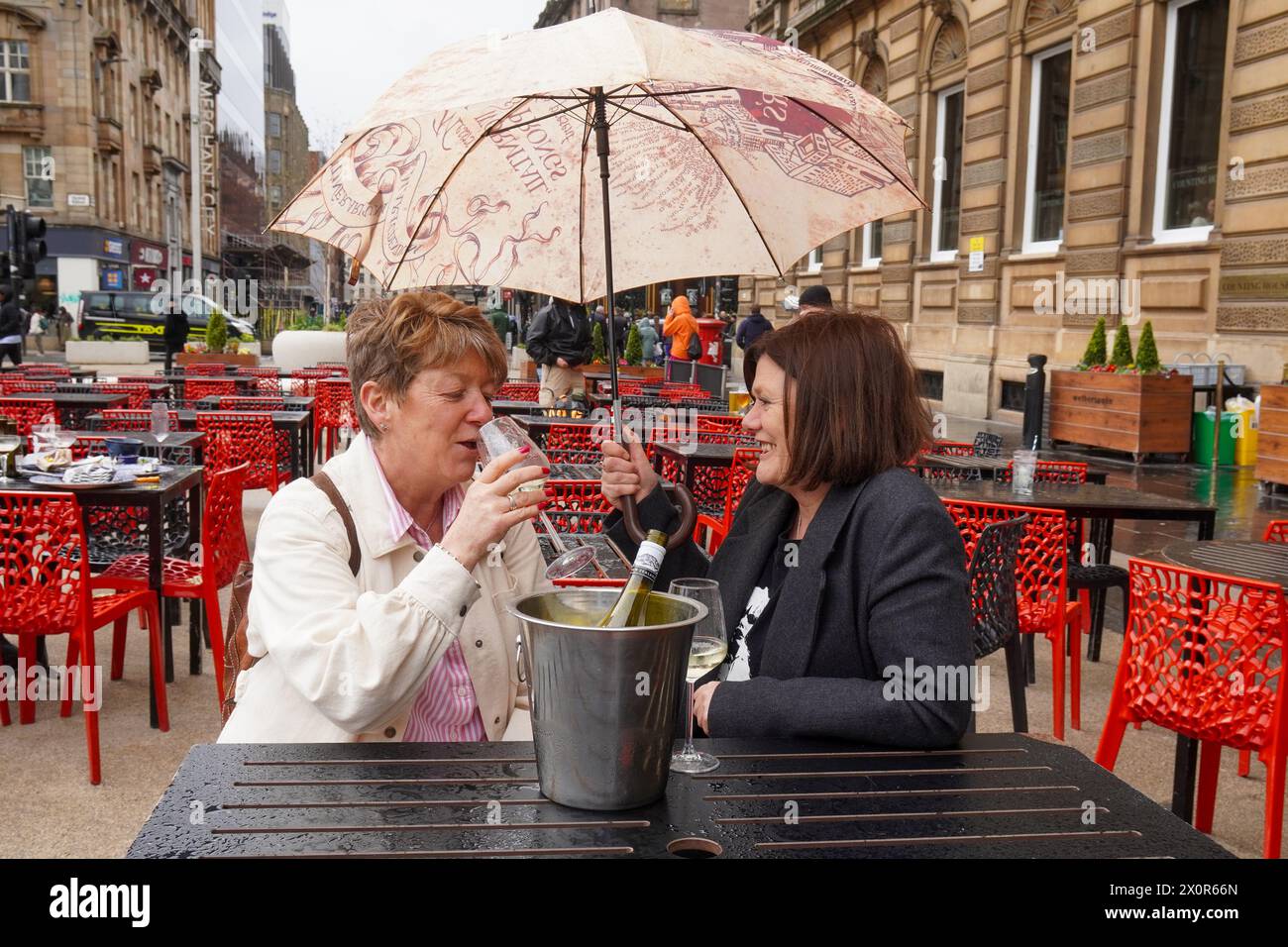Glasgow, Royaume-Uni. 13 avril 2024. Leyanne et Wendy, qui visitent Glasgow depuis Édimbourg, ne sont pas rebutés par le mauvais temps et les fortes pluies, et dégustez un verre de vin, en plein air à George Square, Glasgow, Écosse, Royaume-Uni crédit : Findlay/Alamy Live News Banque D'Images