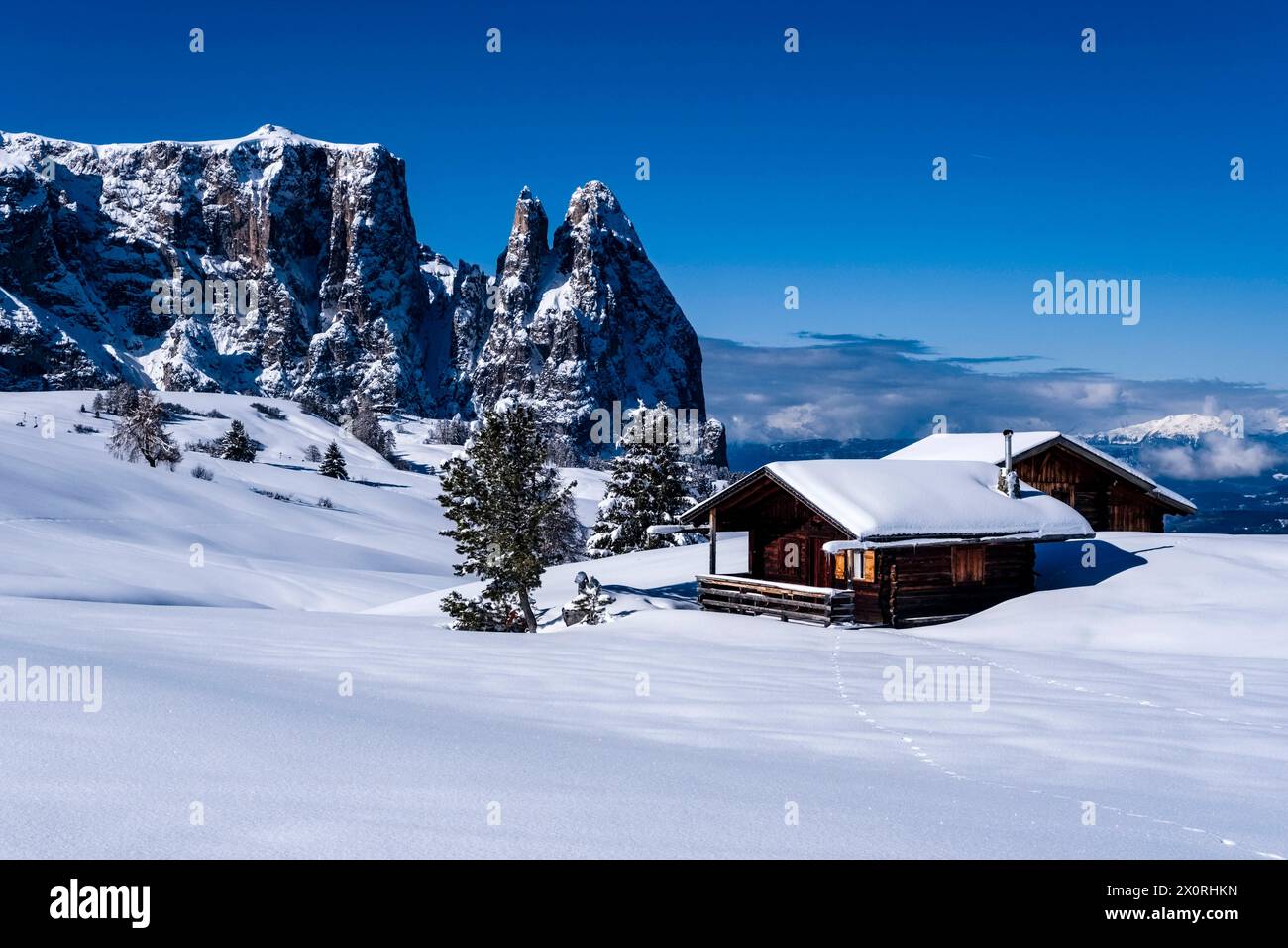 Campagne agricole vallonnée avec pâturages enneigés, arbres et cabanes en bois à Seiser Alm en hiver, sommets de Monte Petz et Sciliar dans le dis Banque D'Images