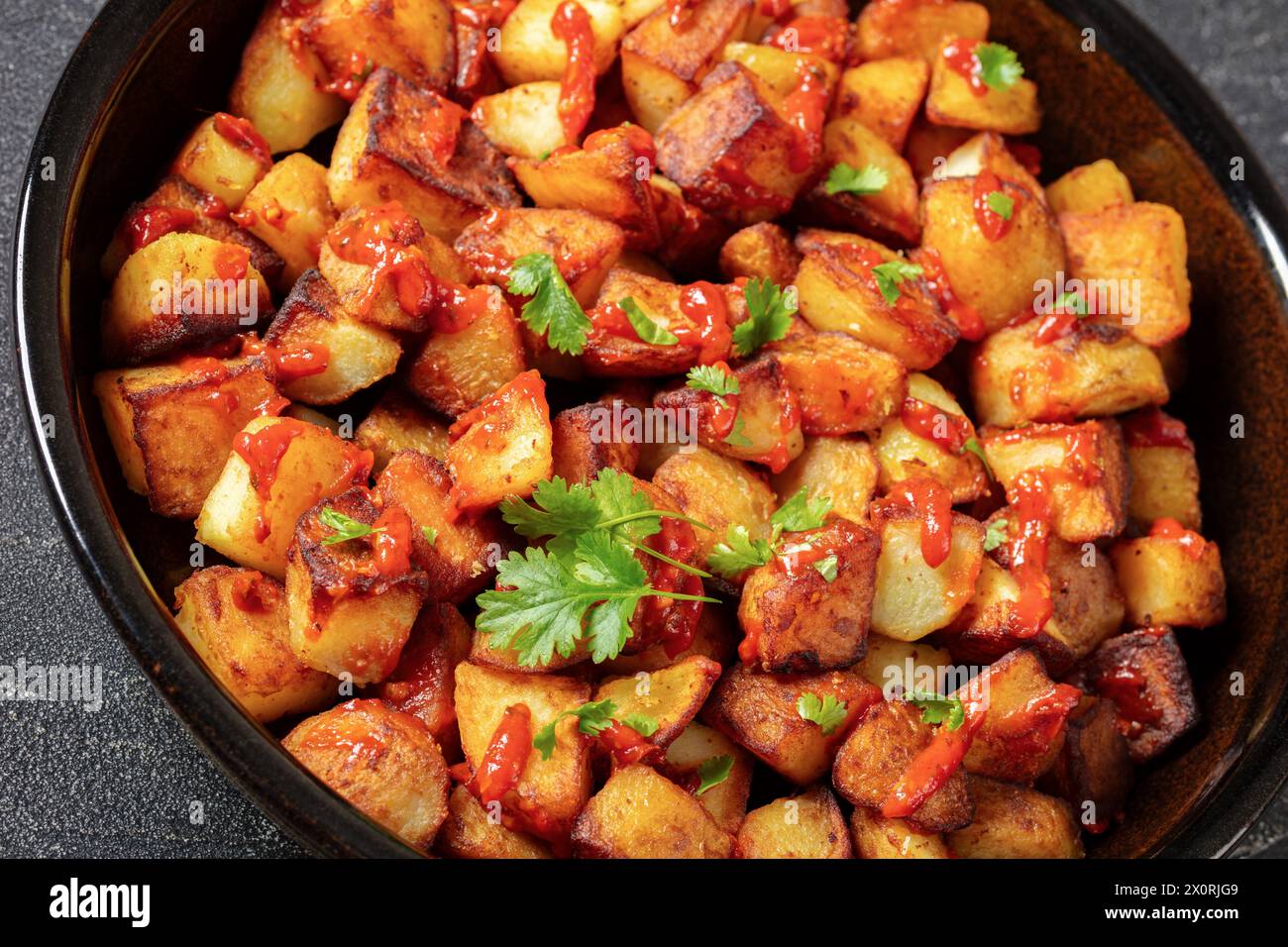 patata bravas frites croustillantes, pommes de terre espagnoles frites avec sauce paprika fumée dans un plat de cuisson sur une table en béton, gros plan Banque D'Images