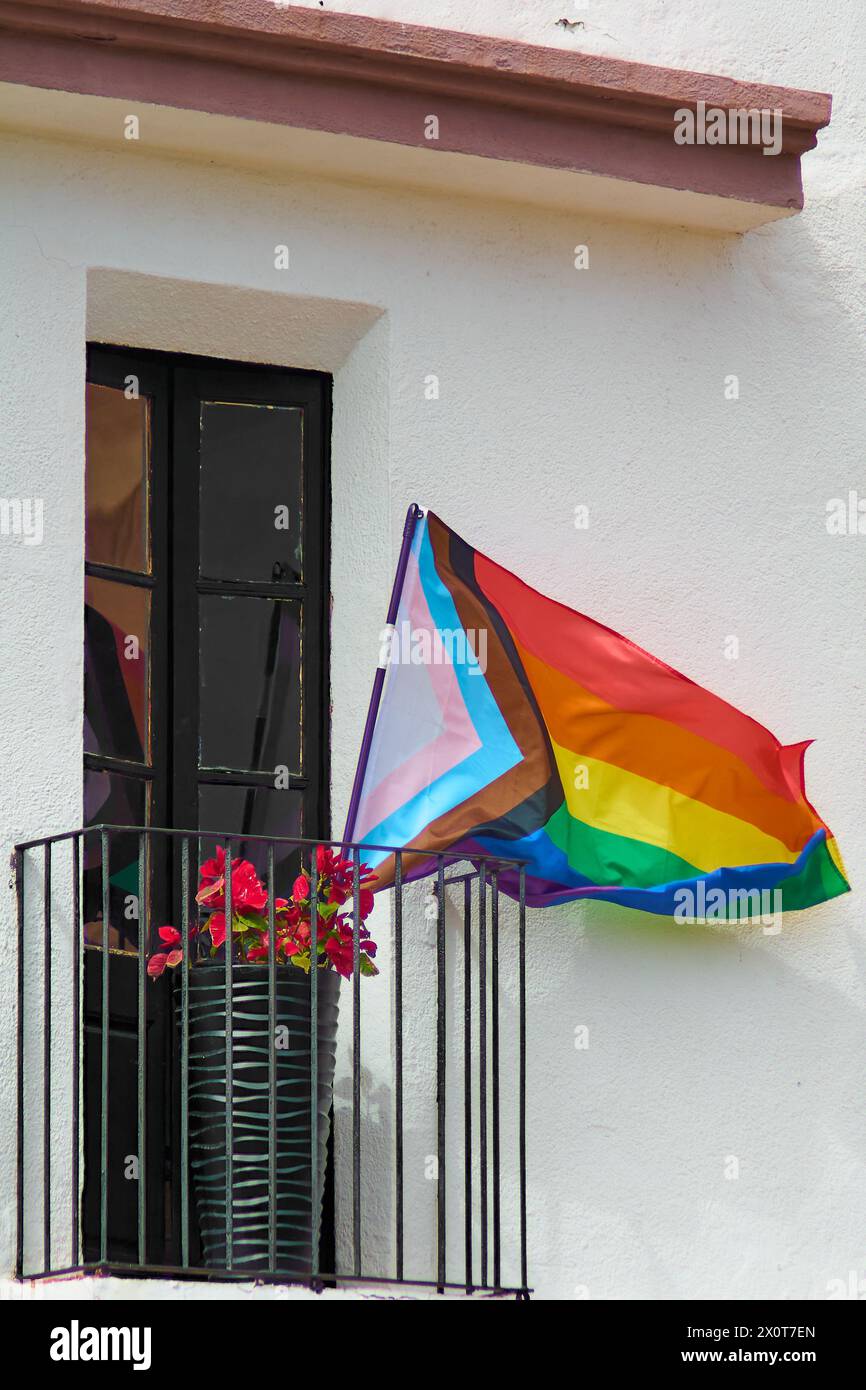 Cette image captivante montre un drapeau arc-en-ciel vibrant, symbolisant la fierté LGBTQ, agitant élégamment sur le fond d'un bâtiment blanc avec un sombre Banque D'Images