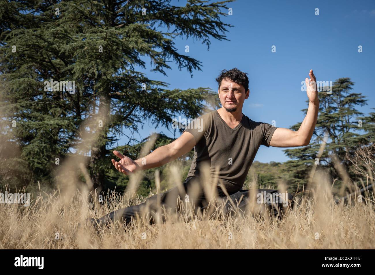 Un homme caucasien d'âge moyen pratique le Kung Fu sur une colline, effectuant des exercices d'étirement, d'équilibre et de force. Banque D'Images
